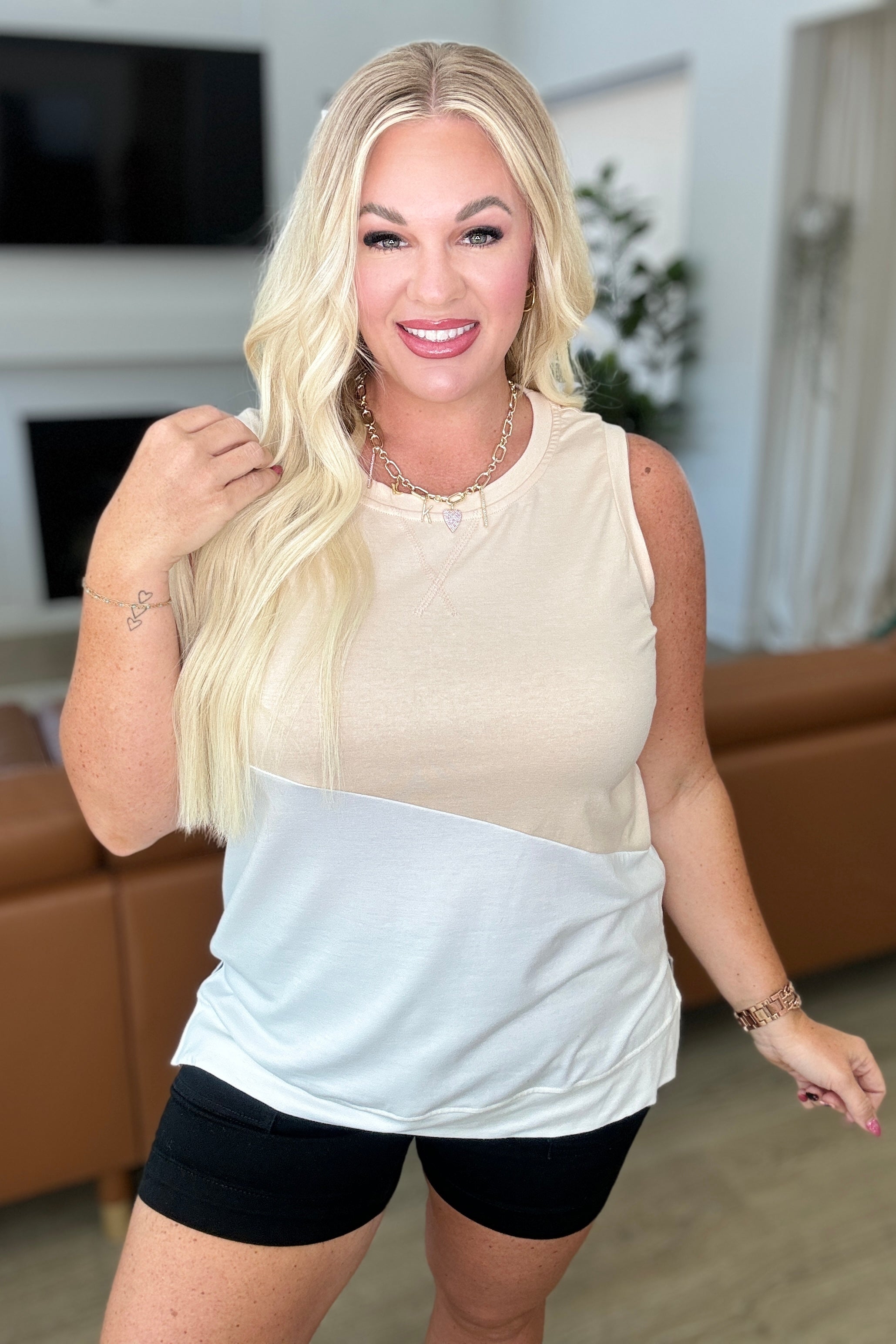 A woman wearing a sleeveless top with a color block design, where the upper part is beige and the lower part is white.