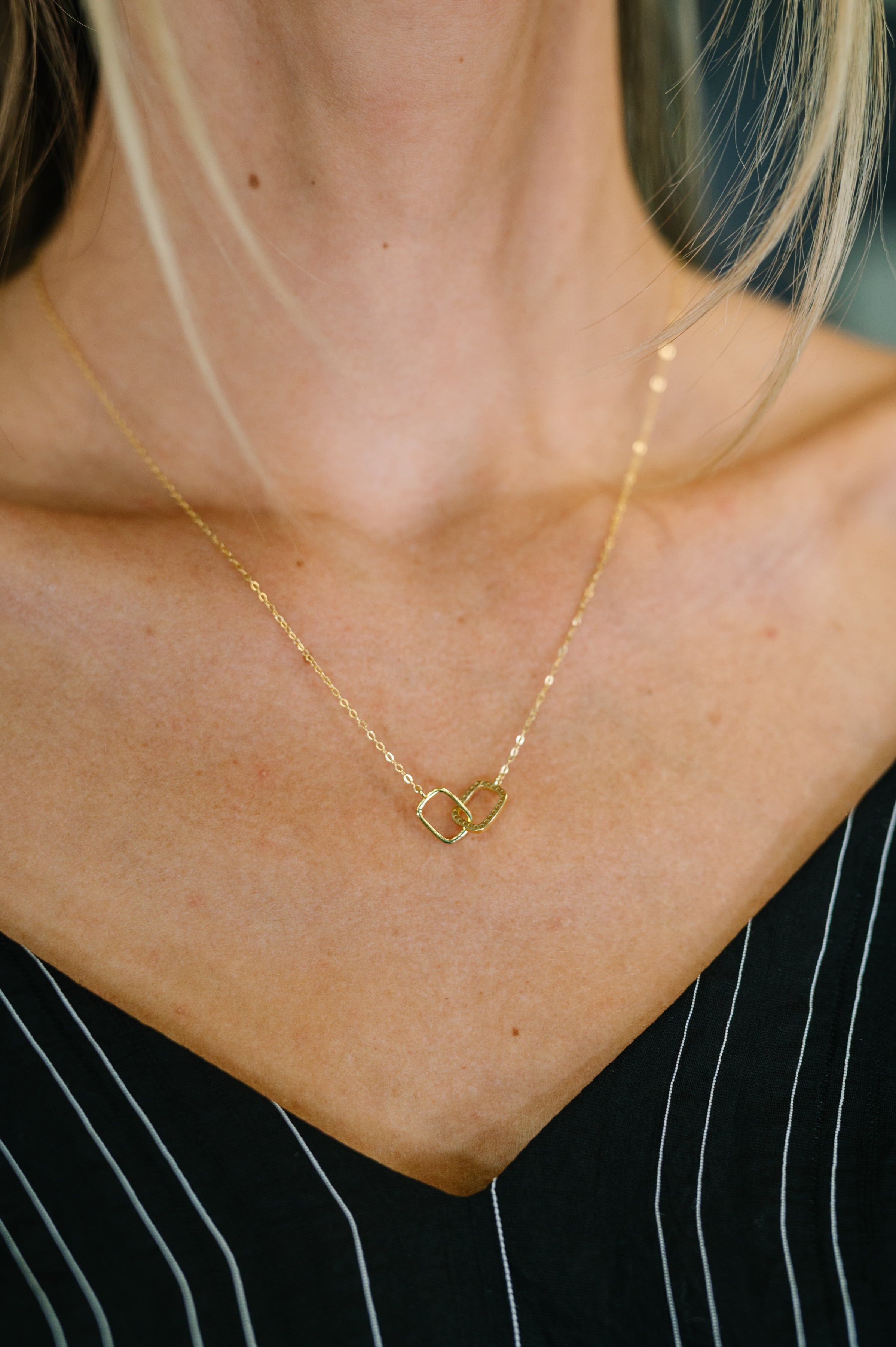 Gold necklace with a pendant on a person wearing a black and white striped shirt.