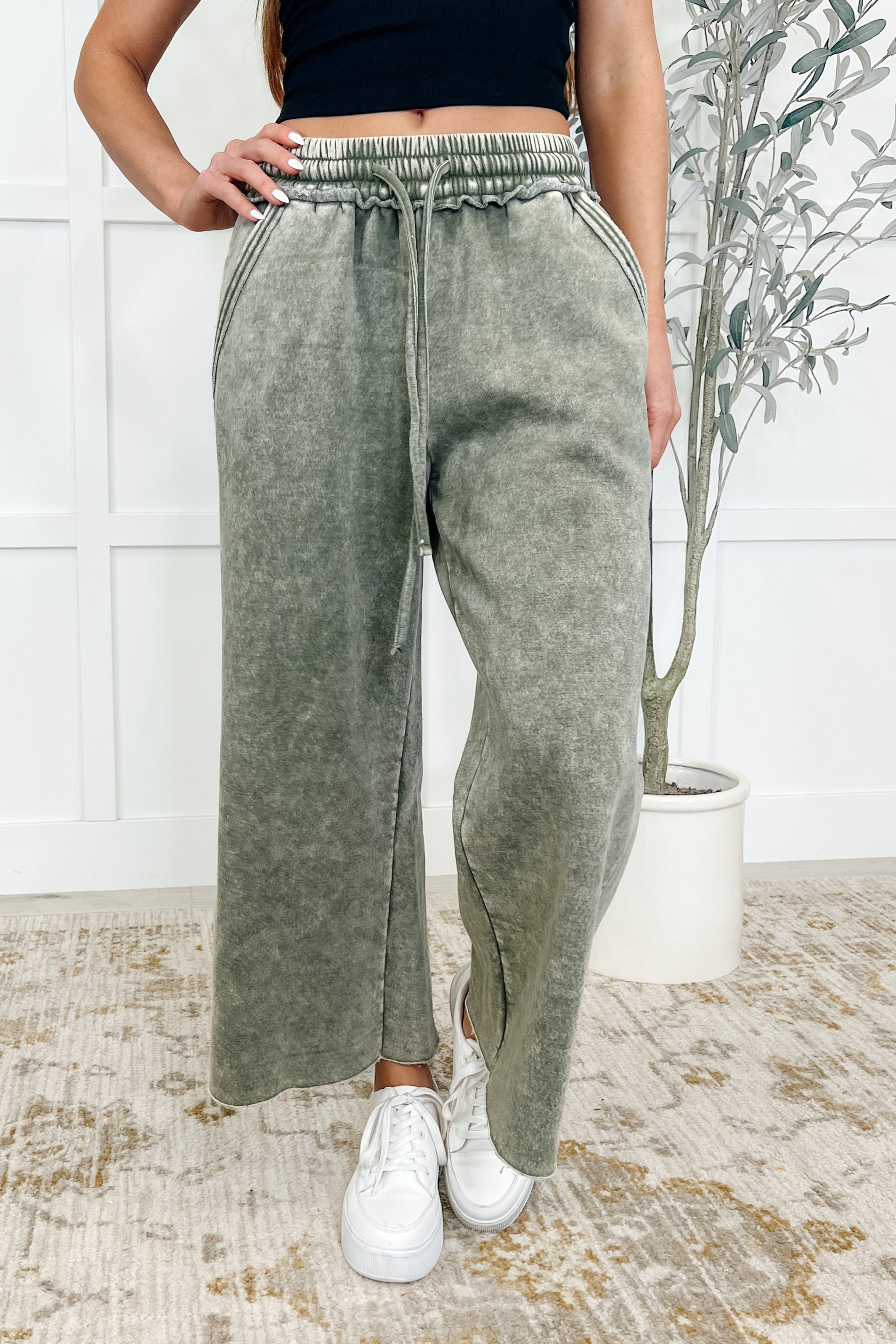 A woman wearing light olive wide leg cropped pants with a cased elastic waistband and side pockets, worn with white sneakers.