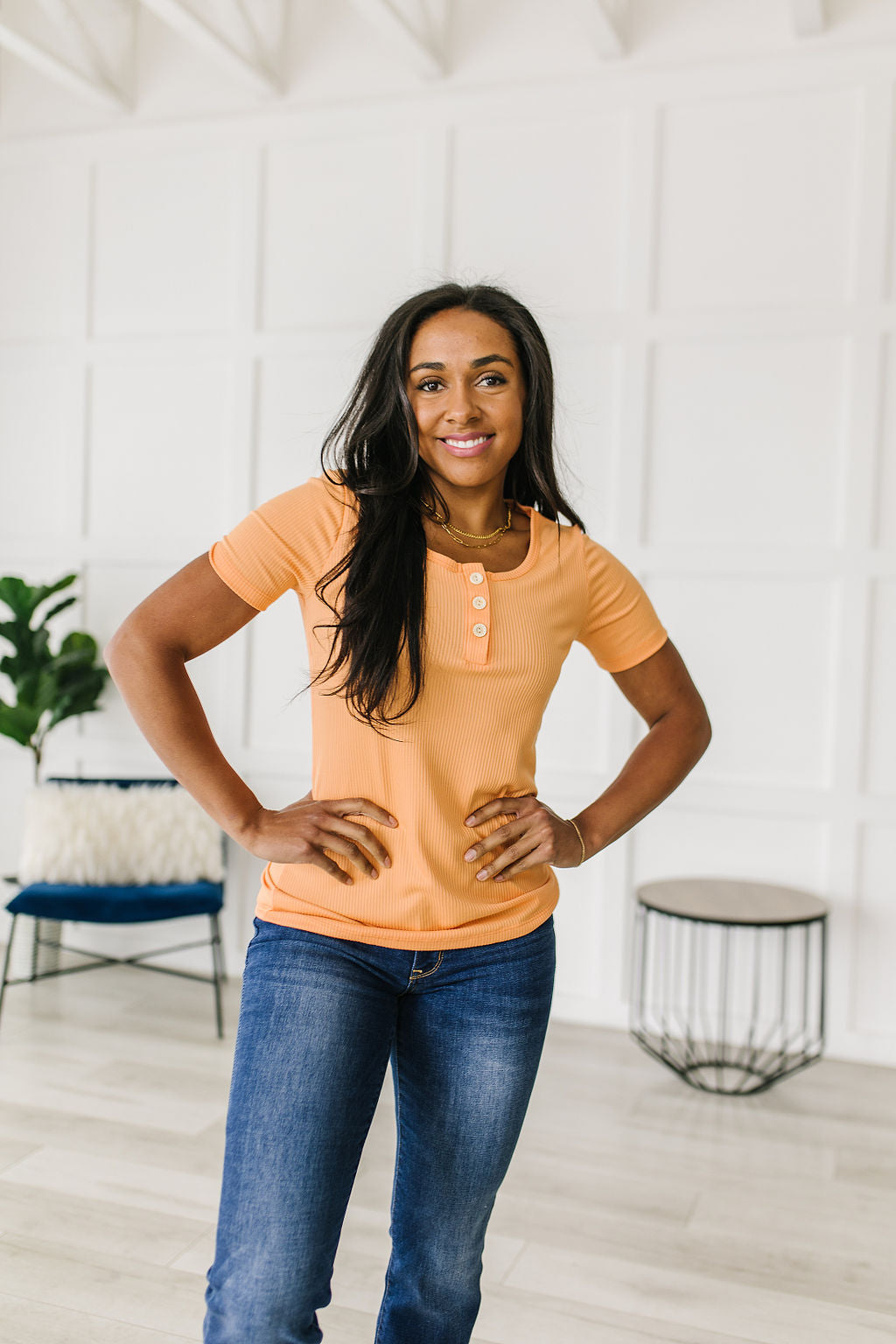 Woman wearing an orange shirt and blue jeans standing in a modern room.