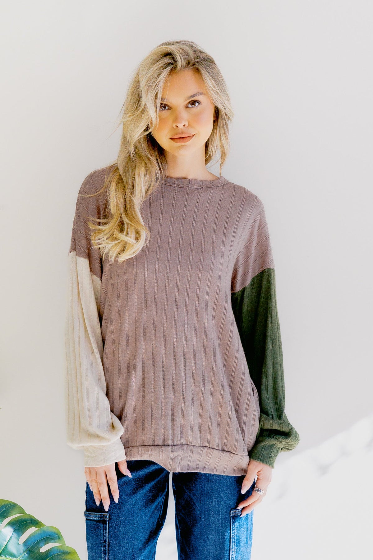 A woman wearing a mocha-colored top with long puff sleeves and a color block design.