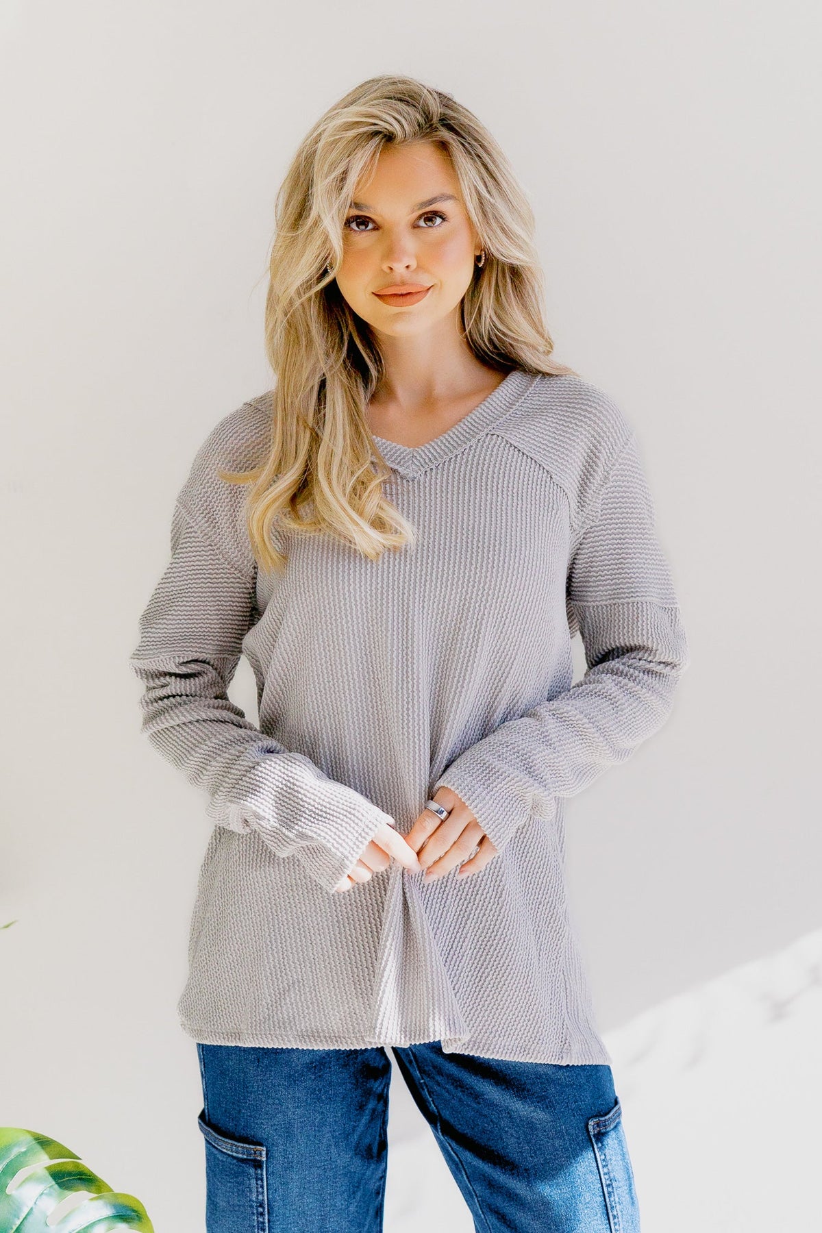 A woman wearing a pearl grey long sleeve knit top with a V-neck and relaxed fit.