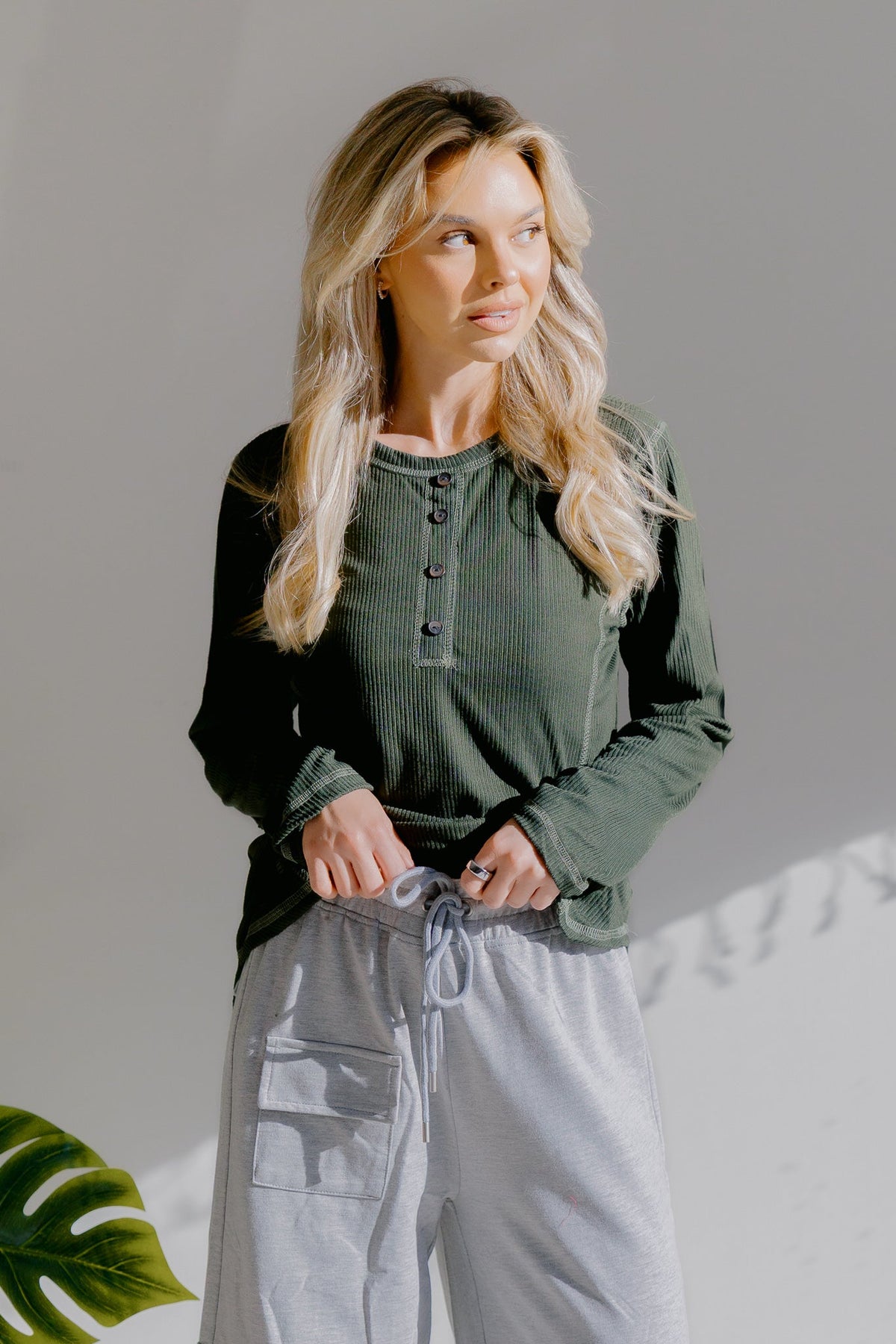 Woman wearing an olive green long-sleeve henley top with button details.