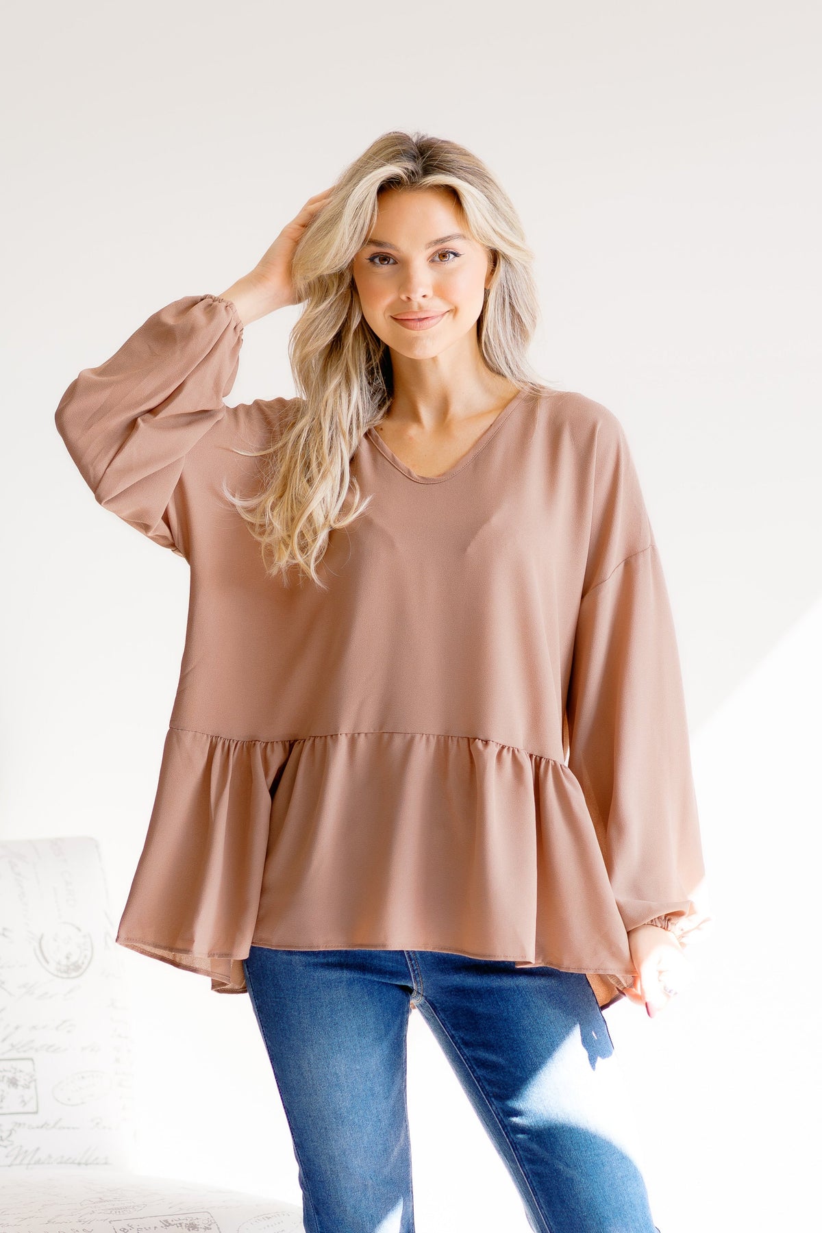A mocha-colored peplum top with balloon sleeves, worn by a woman standing indoors.