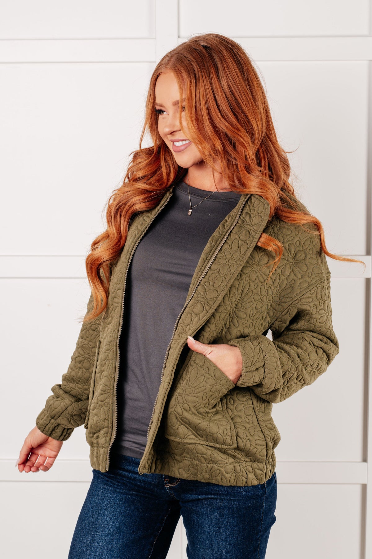 A woman wearing an olive quilted zip-up jacket with a standing collar and patch pockets.