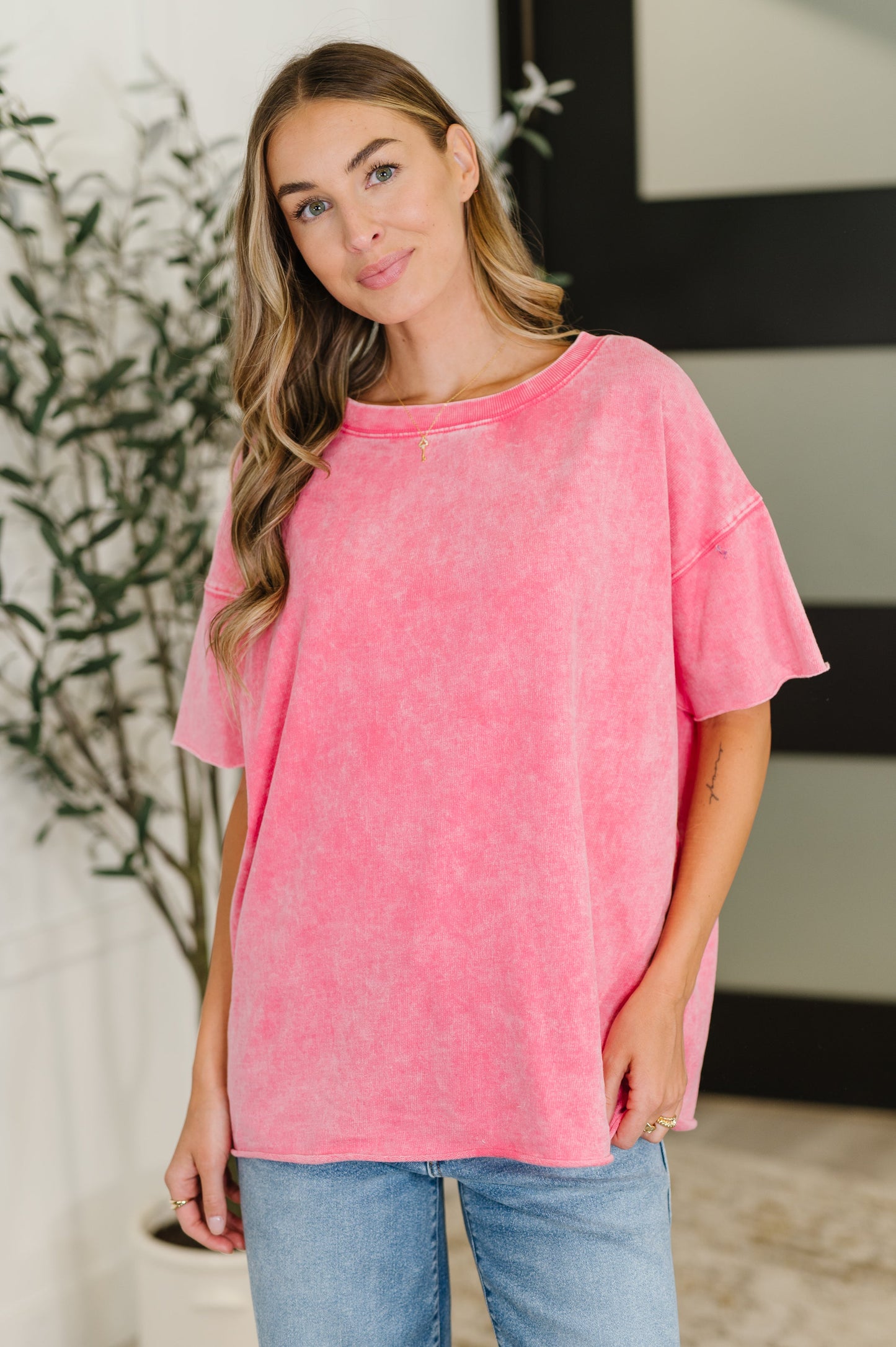 Woman wearing a pink oversized t-shirt and blue jeans indoors.