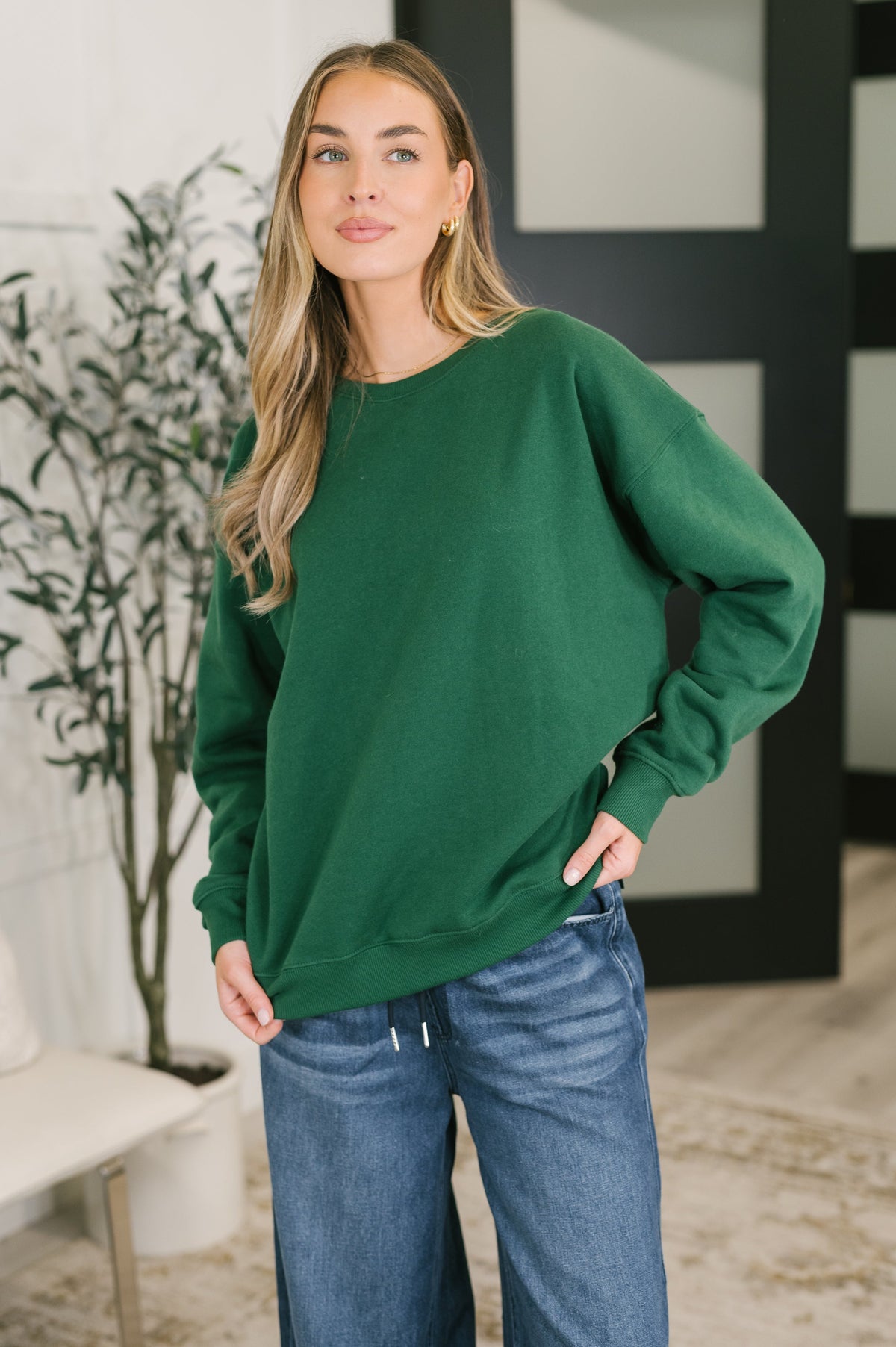 Green drop shoulder pullover with ribbed neckline and cuffs, worn by a person with blue jeans.