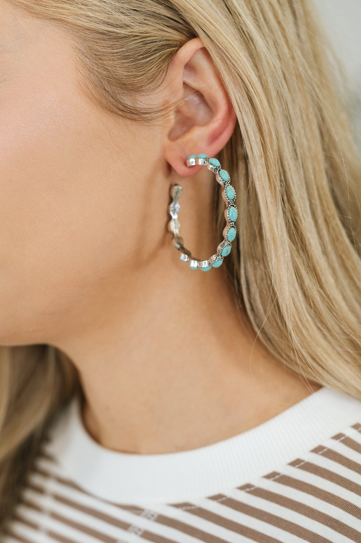 Turquoise gem-inlaid C-shape hoop earrings with push-back closure on a person's ear.