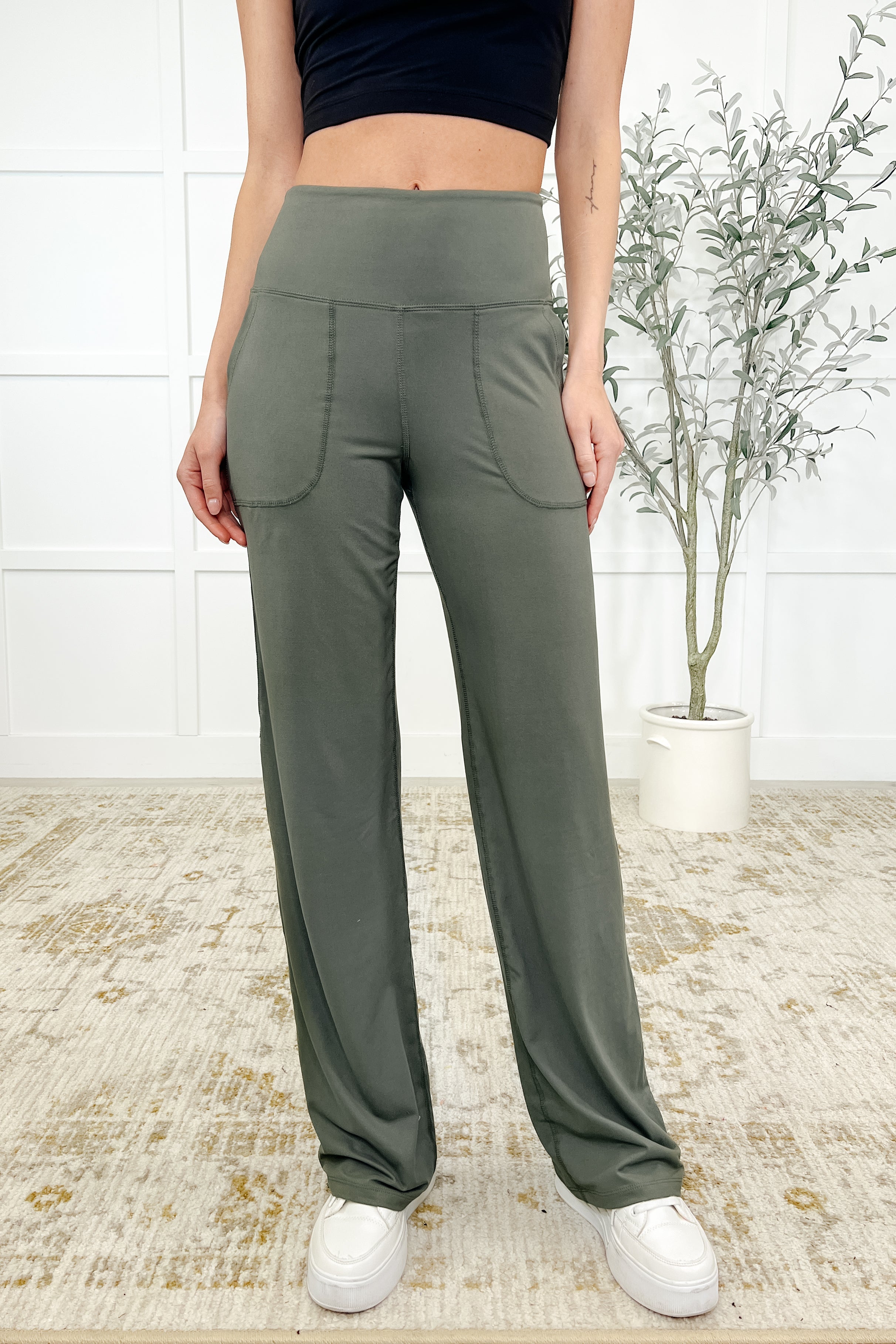 A woman wearing green straight leg bottoms with an exaggerated banded waistband, functional patch pockets, and a contour booty seam.