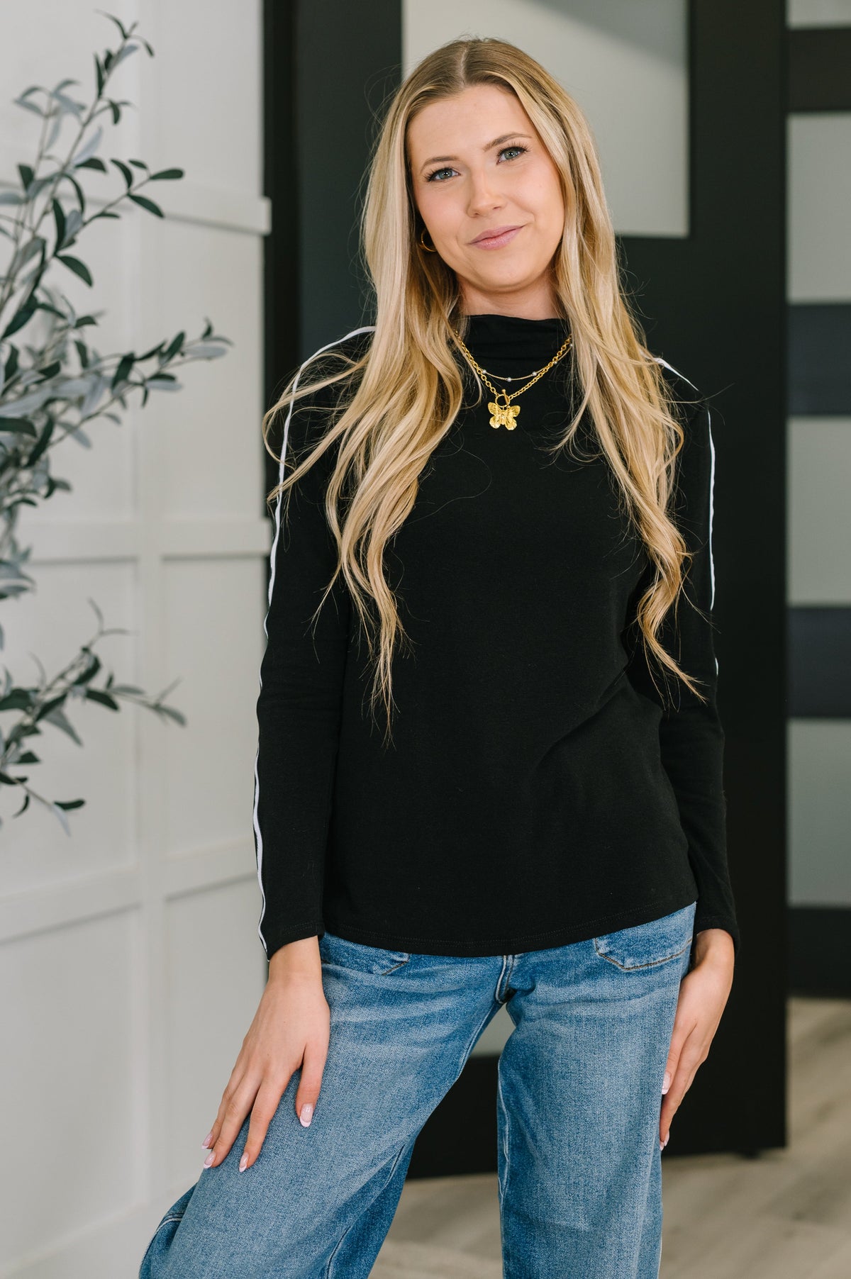 A woman wearing a black high neck pullover with long sleeves and ribbon detail.