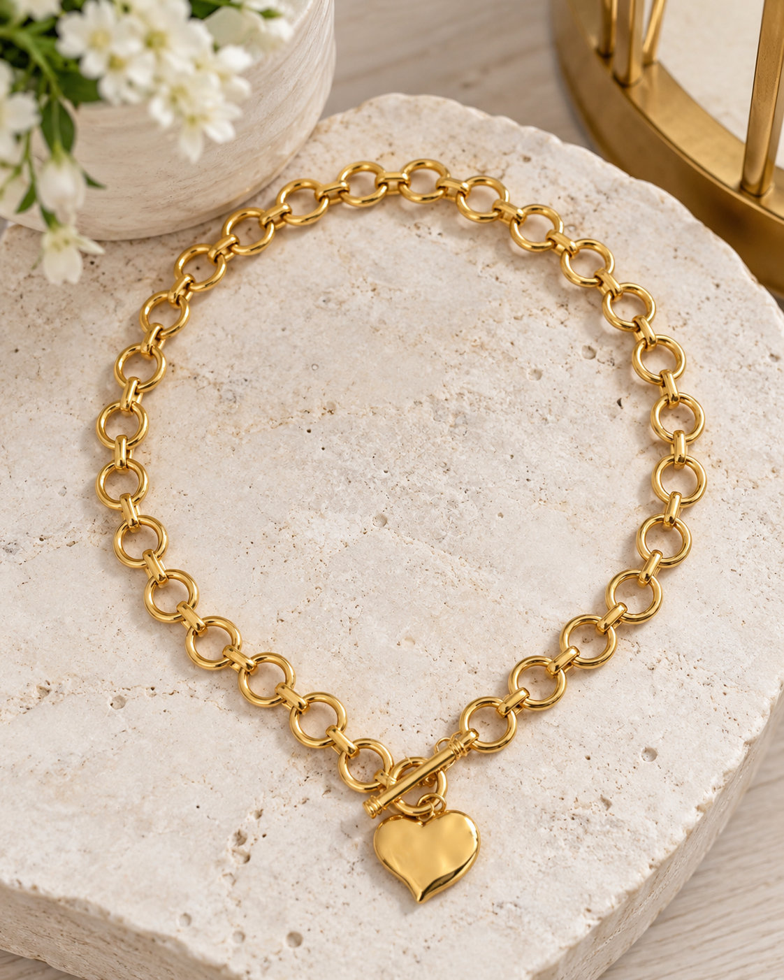Gold necklace with a hammered heart pendant and toggle clasp on a stone surface.