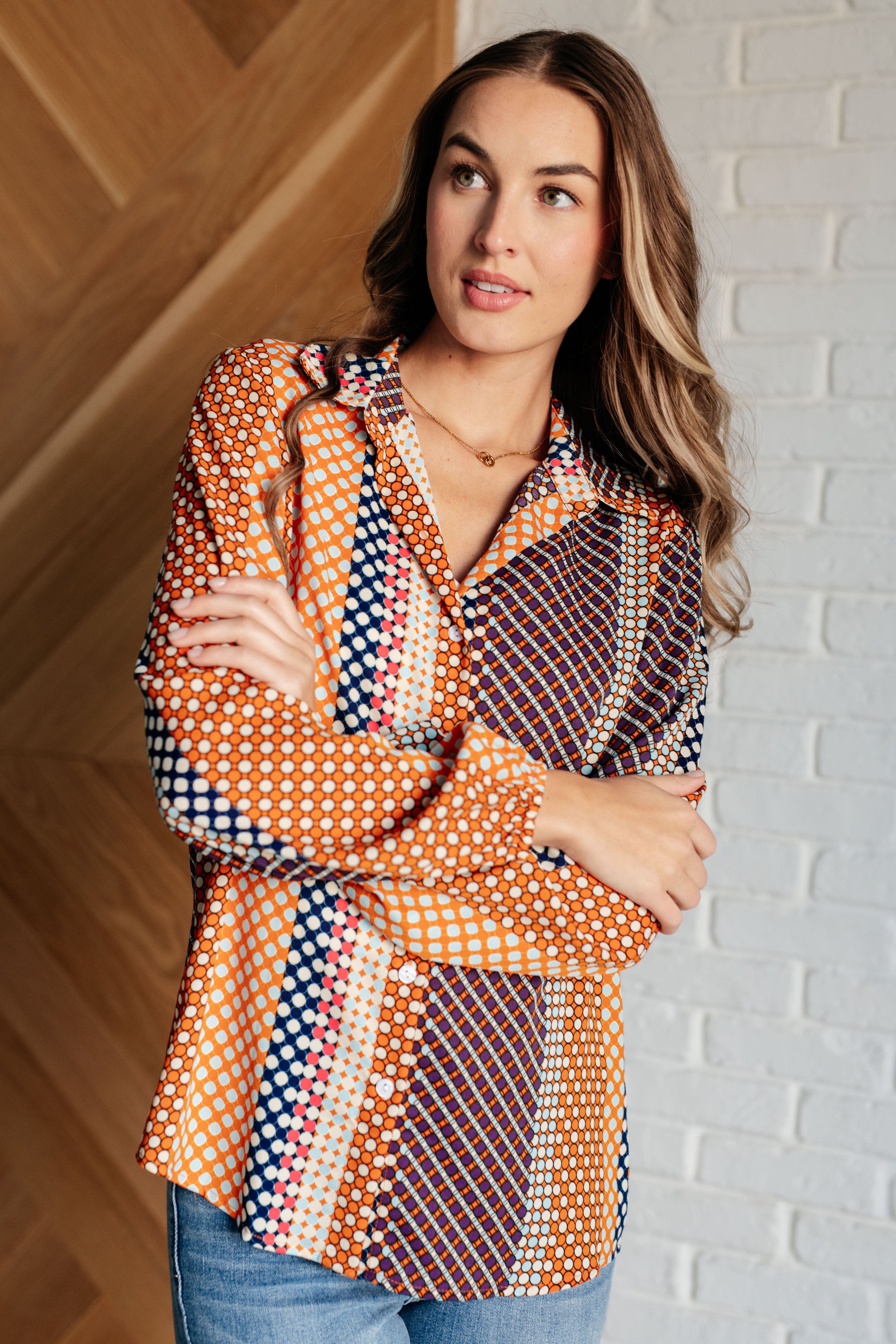 Woman wearing a colorful patterned blouse against a brick wall.