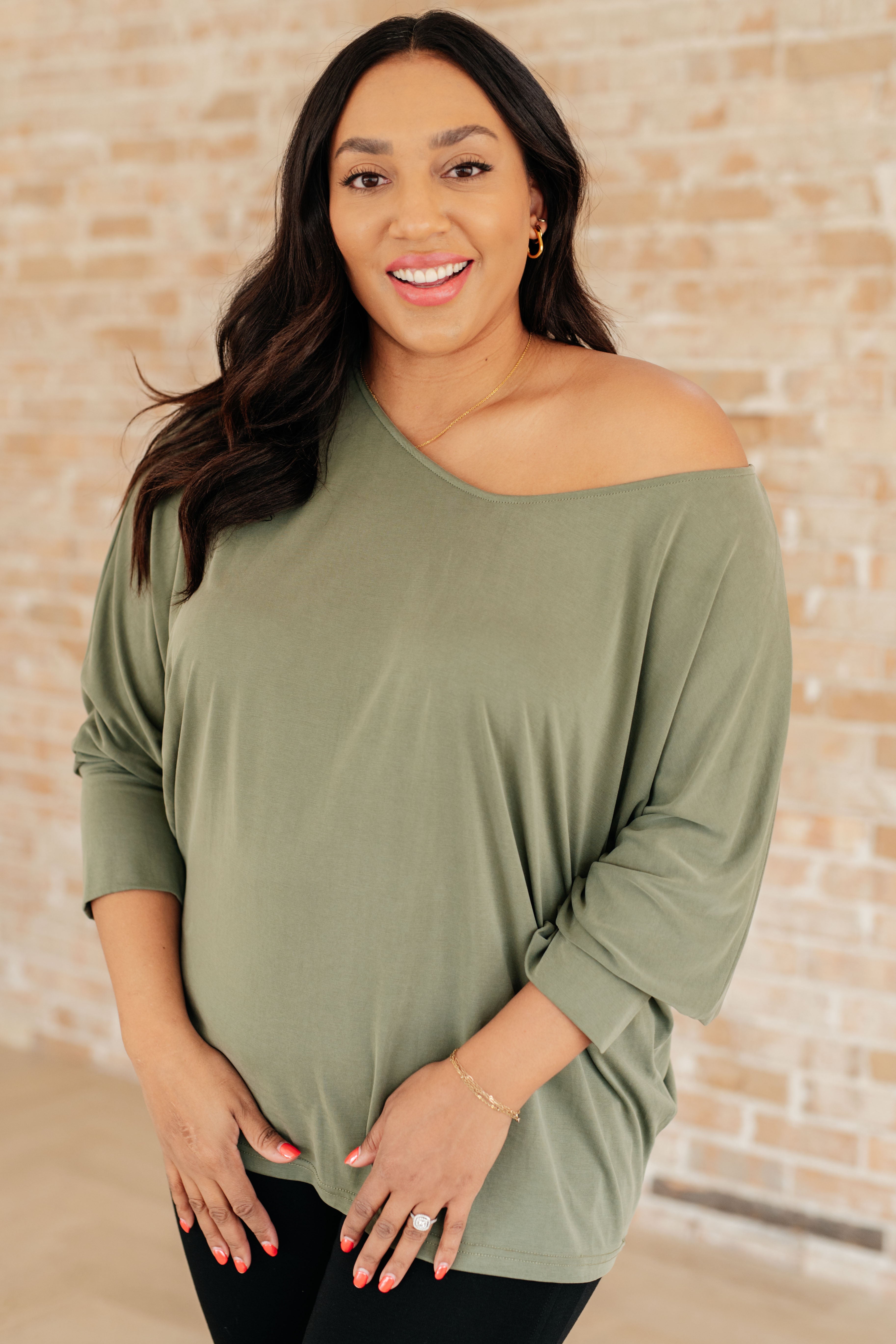 Olive long sleeve top with a boat neckline and dolman sleeves, worn by a smiling model.