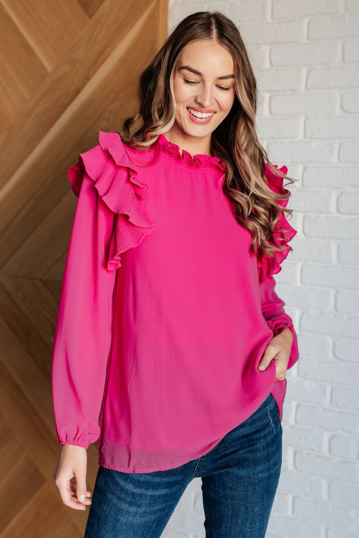 A woman wearing a pink top with ruffles and balloon sleeves, styled with jeans.