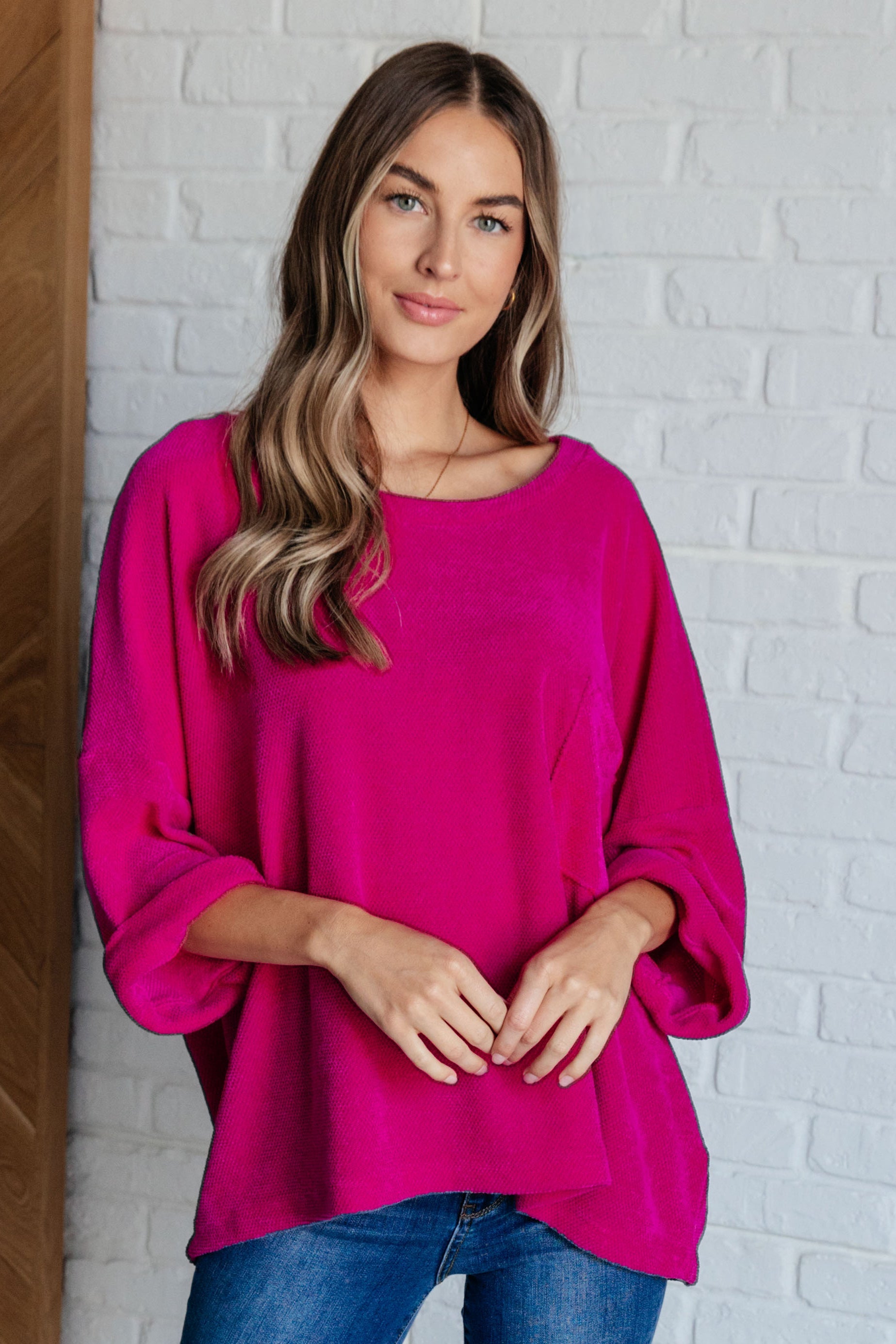 Woman wearing a bright pink sweater against a white brick wall