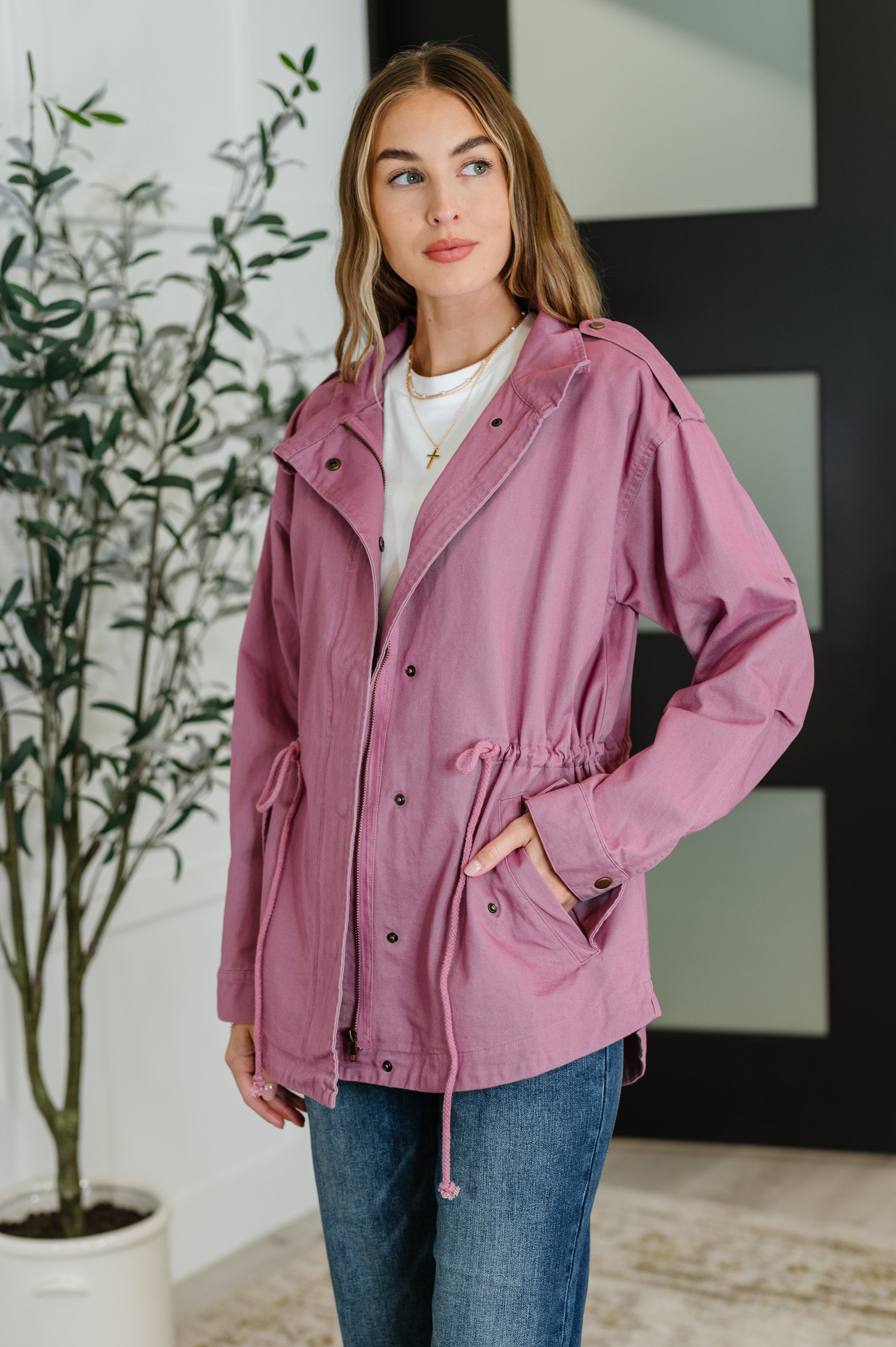 Woman wearing a mauve jacket indoors with a plant in the background