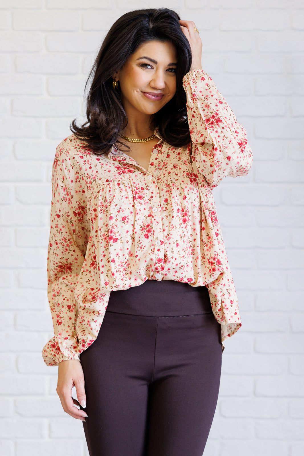 Woman wearing a floral blouse and dark pants against a white brick wall