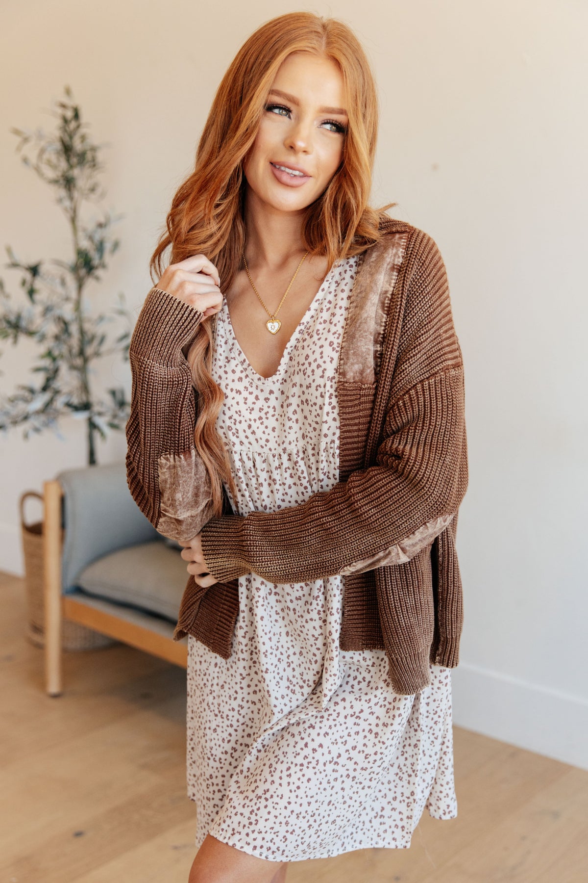 A brown cardigan with open front, woven accents, and ribbed cuffs worn over a patterned dress.