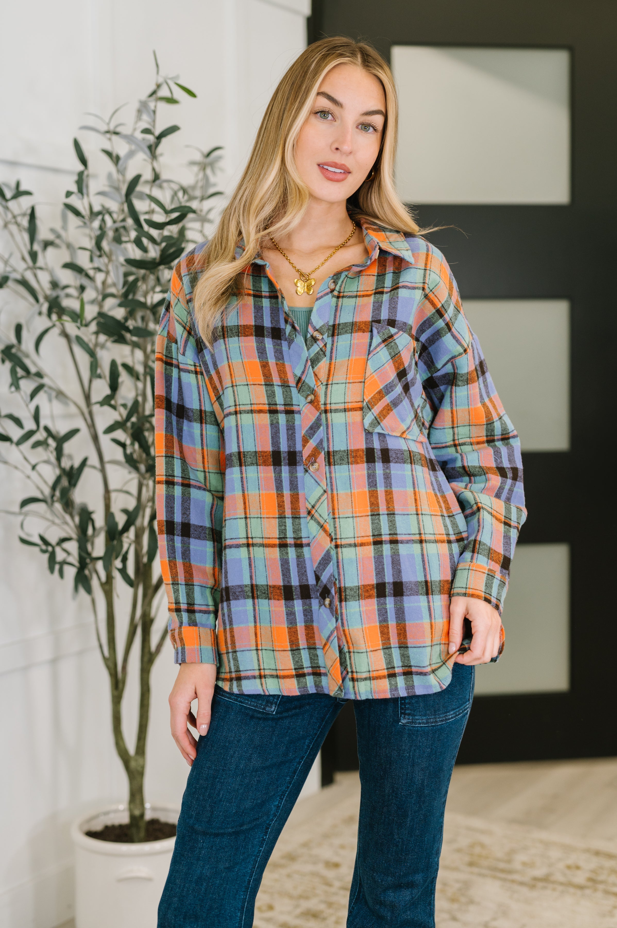 A woman wearing a multicolor plaid button-down shirt with a collared neckline and front pockets.