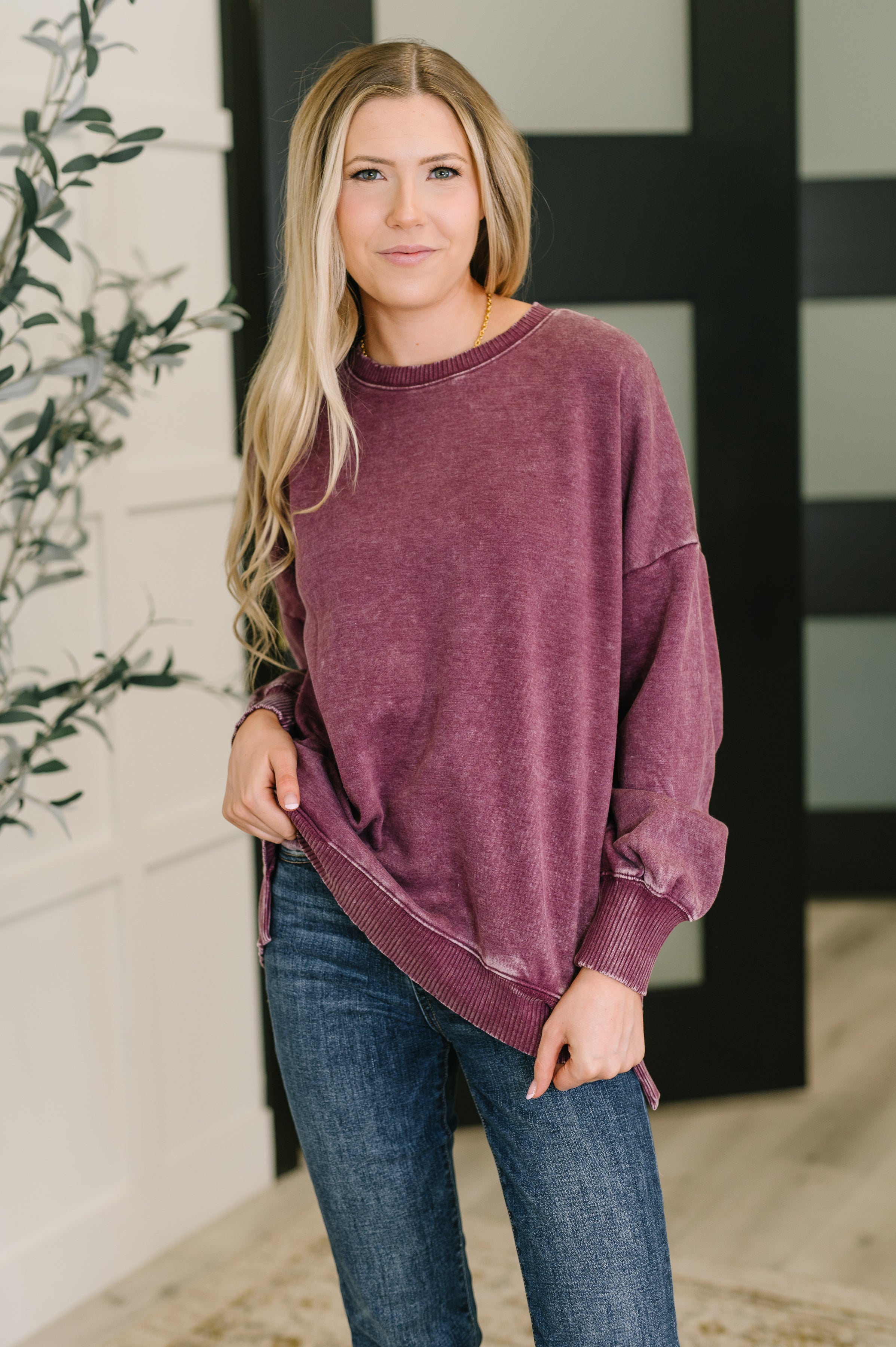 Woman wearing a purple sweatshirt and blue jeans standing against a neutral background