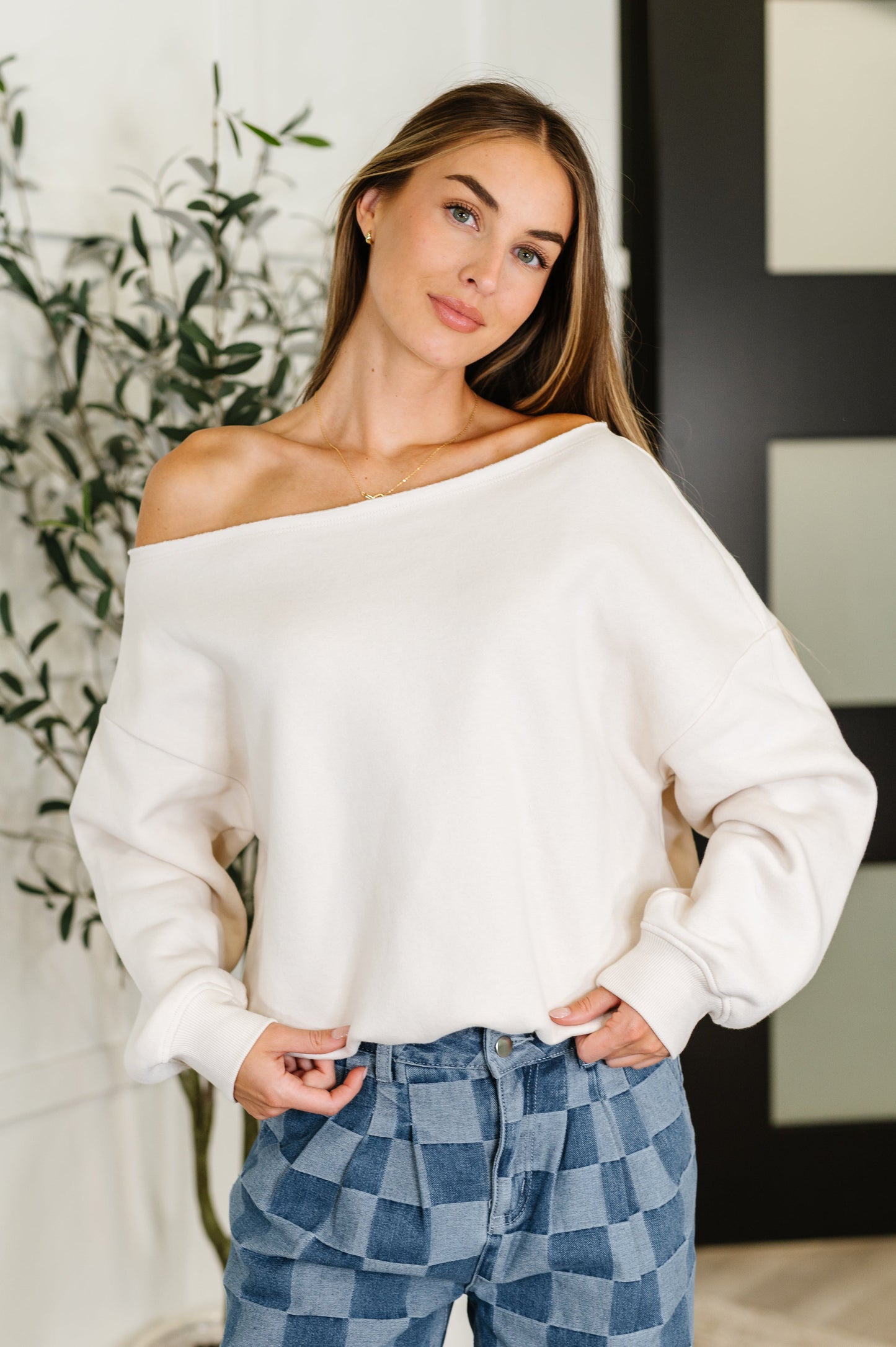Woman wearing a white off-shoulder long sleeve shirt top and blue checkered pants indoors.