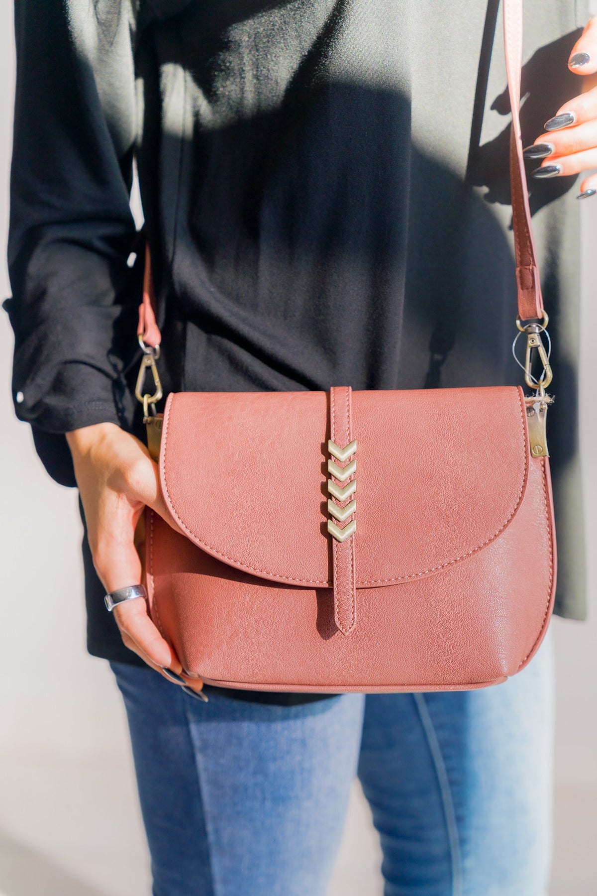 Pink crossbody bag with silky faux leather finish and a decorative strap accent.
