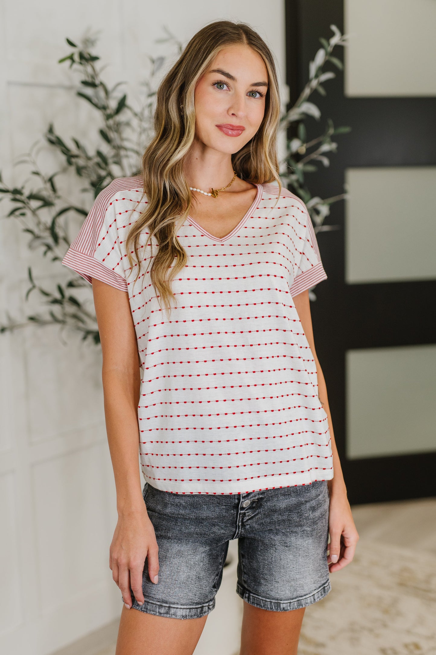 Woman wearing a striped shirt and denim shorts standing indoors with decorative elements in the background