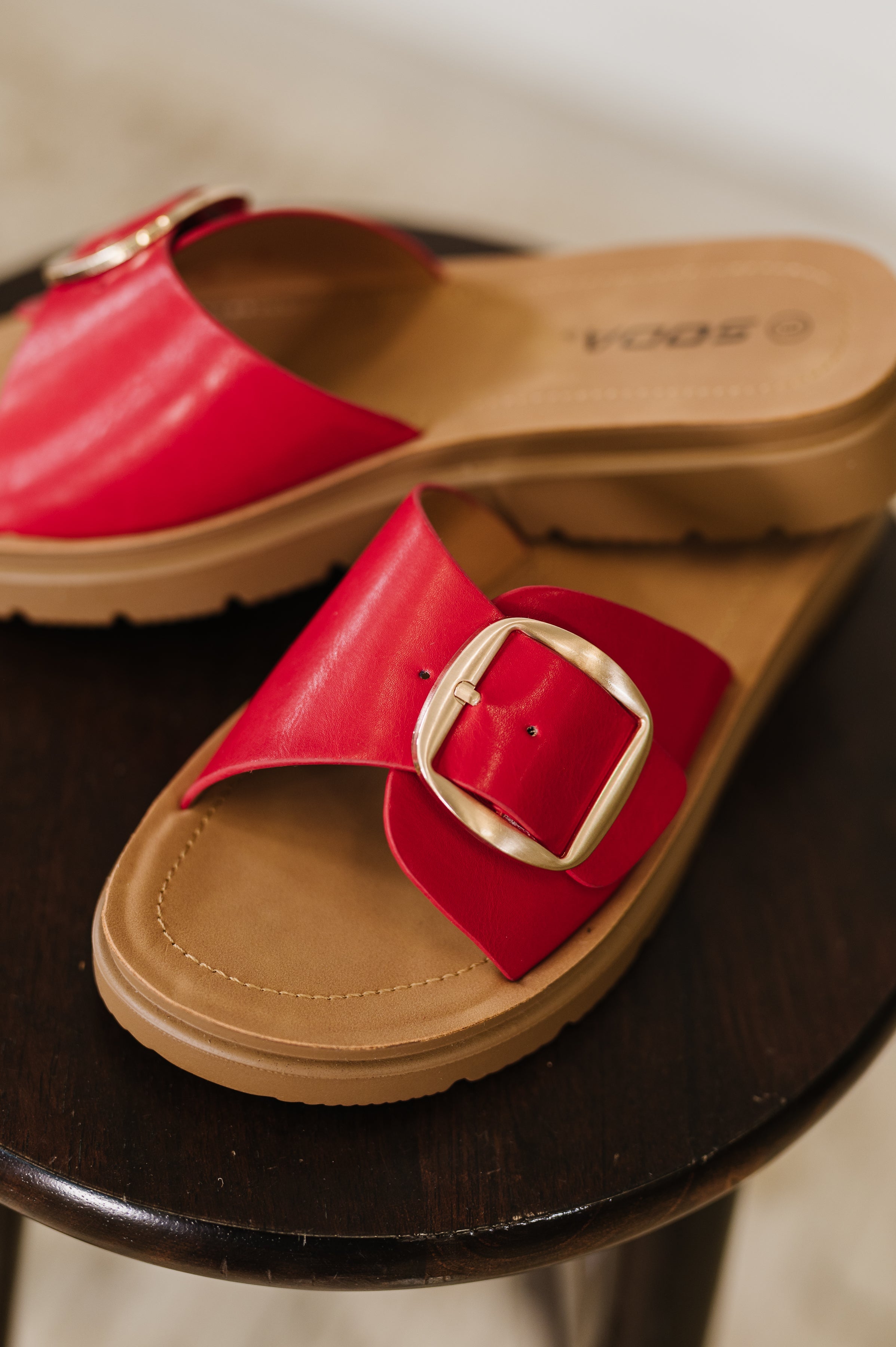 Red slide sandals with a gold buckle on a black surface