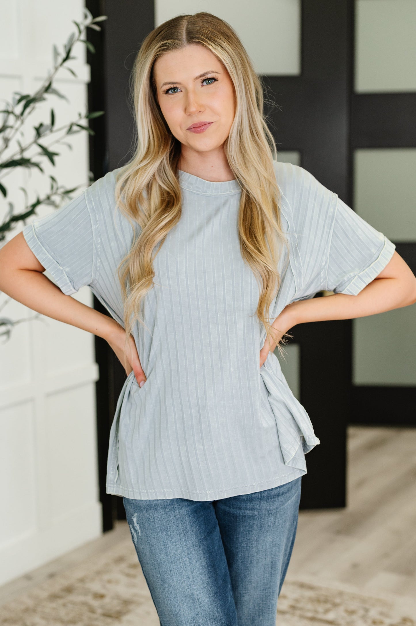 Woman wearing a light gray ribbed top and jeans indoors.