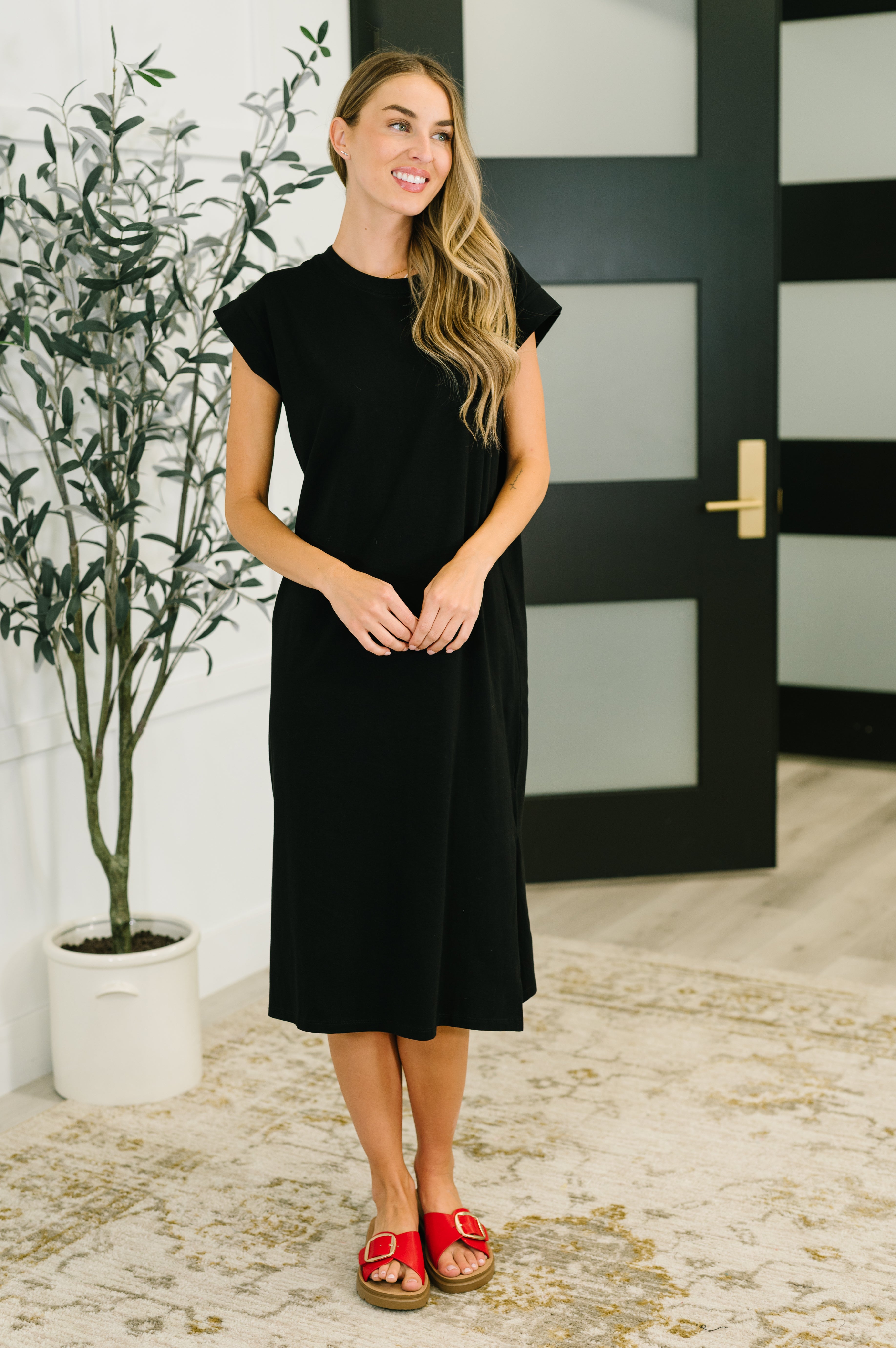 Woman wearing a black dress standing in a room with a plant and door in the background