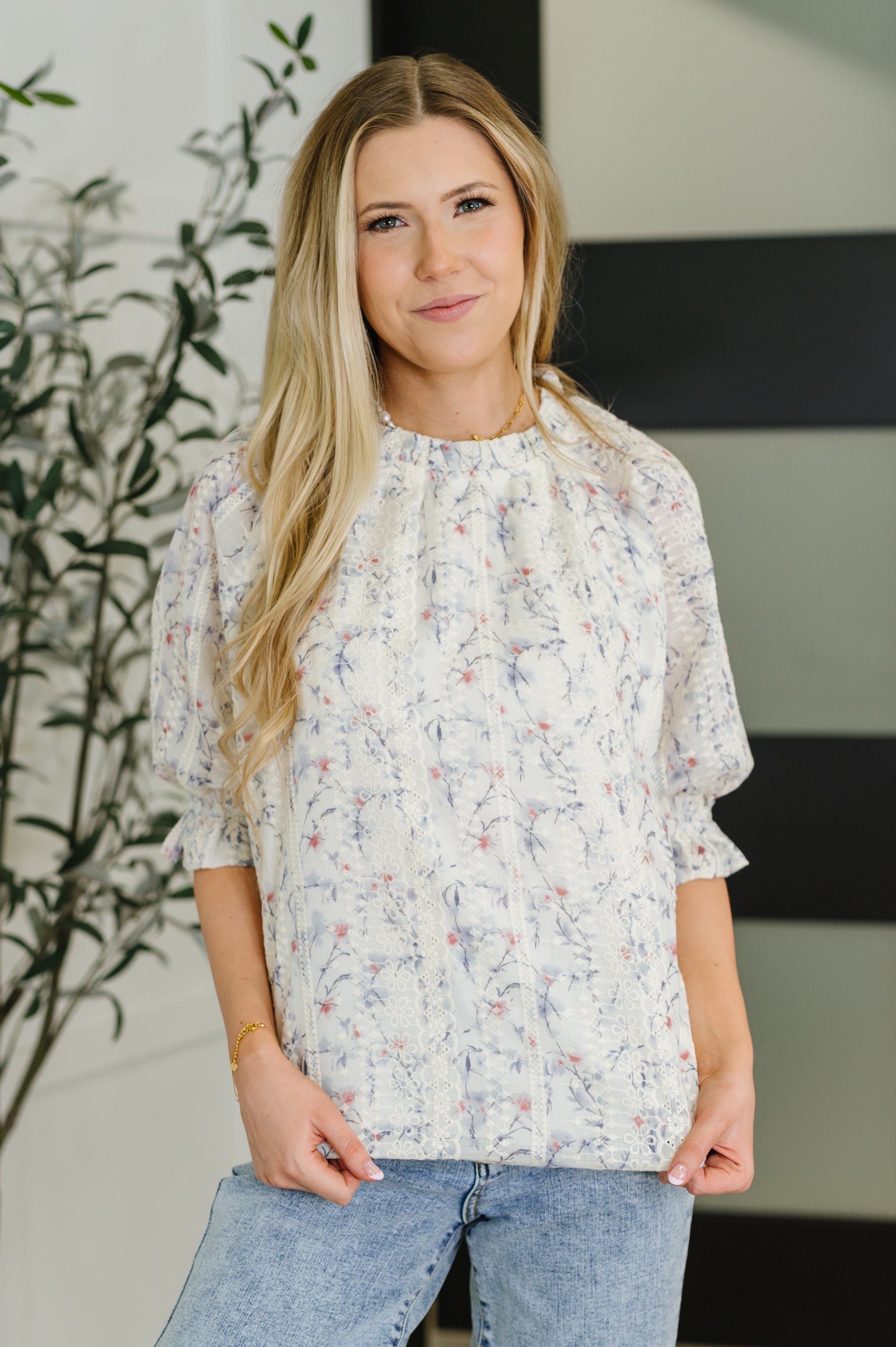 Woman wearing a floral blouse and jeans indoors with a plant in the background