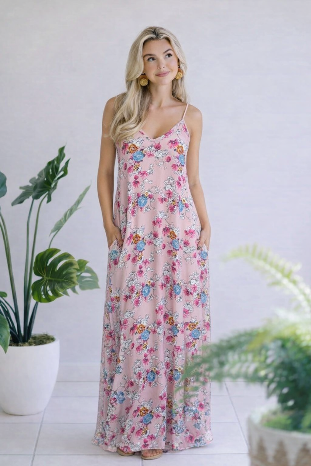 Maxi dress in dusty pink with floral print, v-neckline, spaghetti straps, and side pockets.