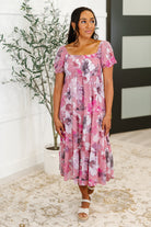 Woman wearing a pink floral dress standing indoors with a plant in the background