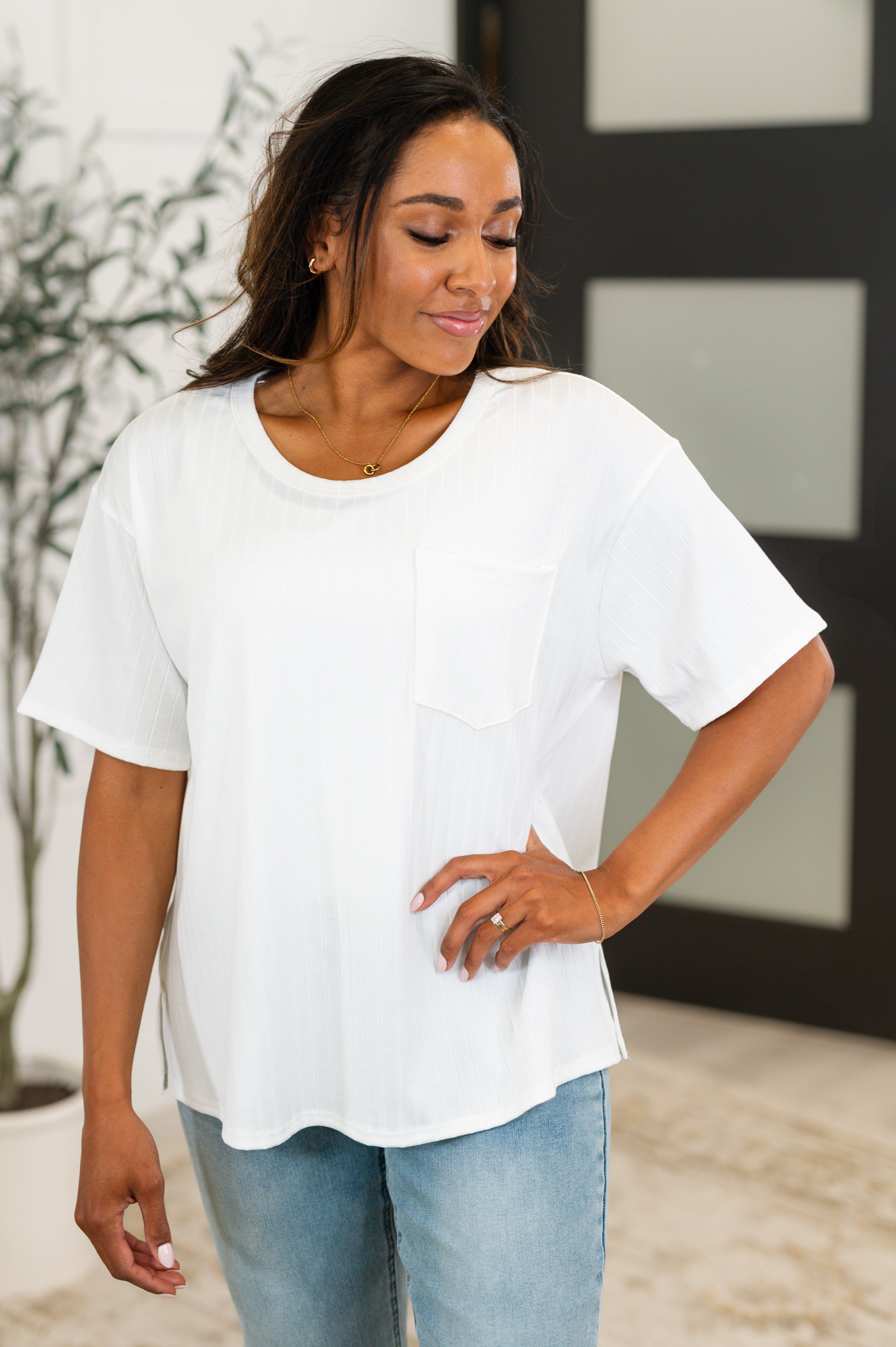 A woman wearing a white slouchy tee with a round neckline, front pocket, and side slits paired with blue jeans.