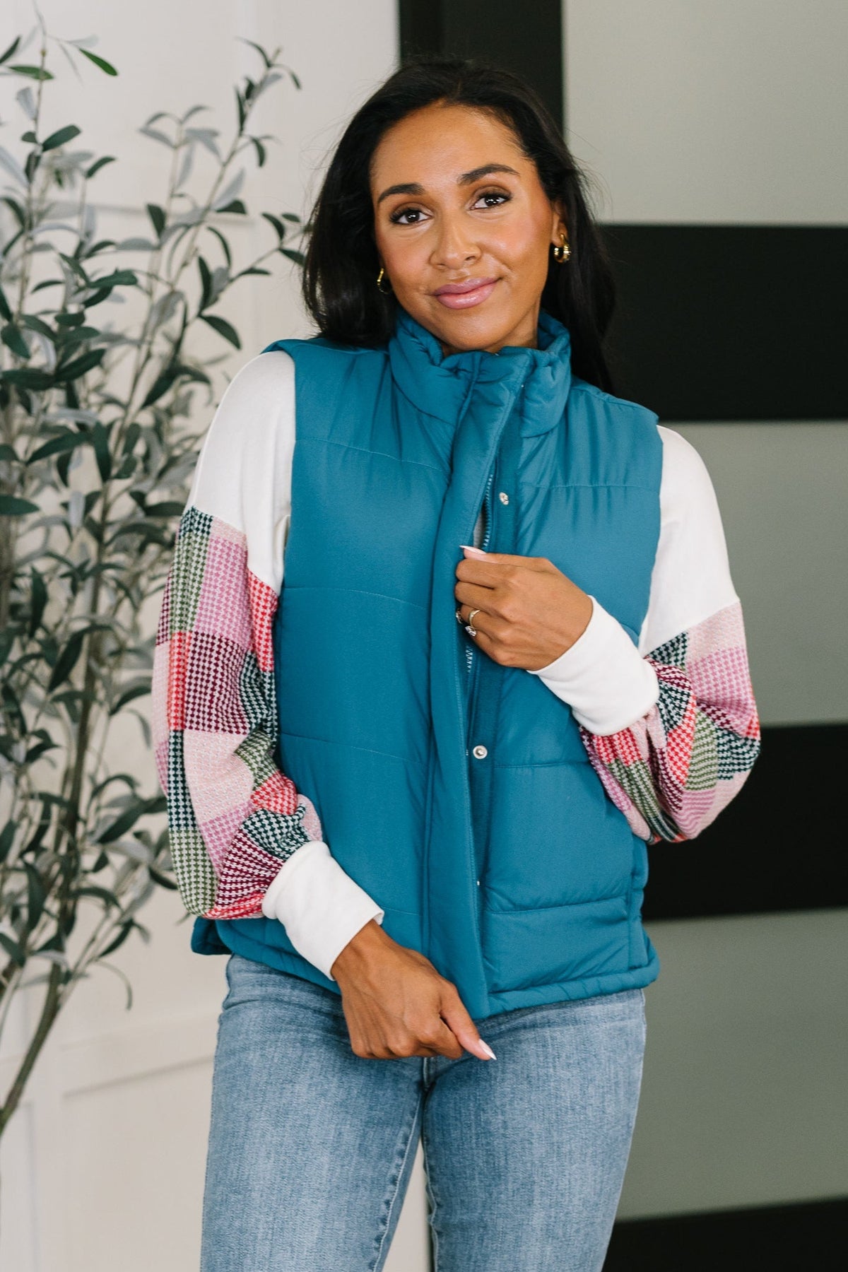 A woman wearing a teal puffer vest with a high neck and full front zipper, standing indoors.