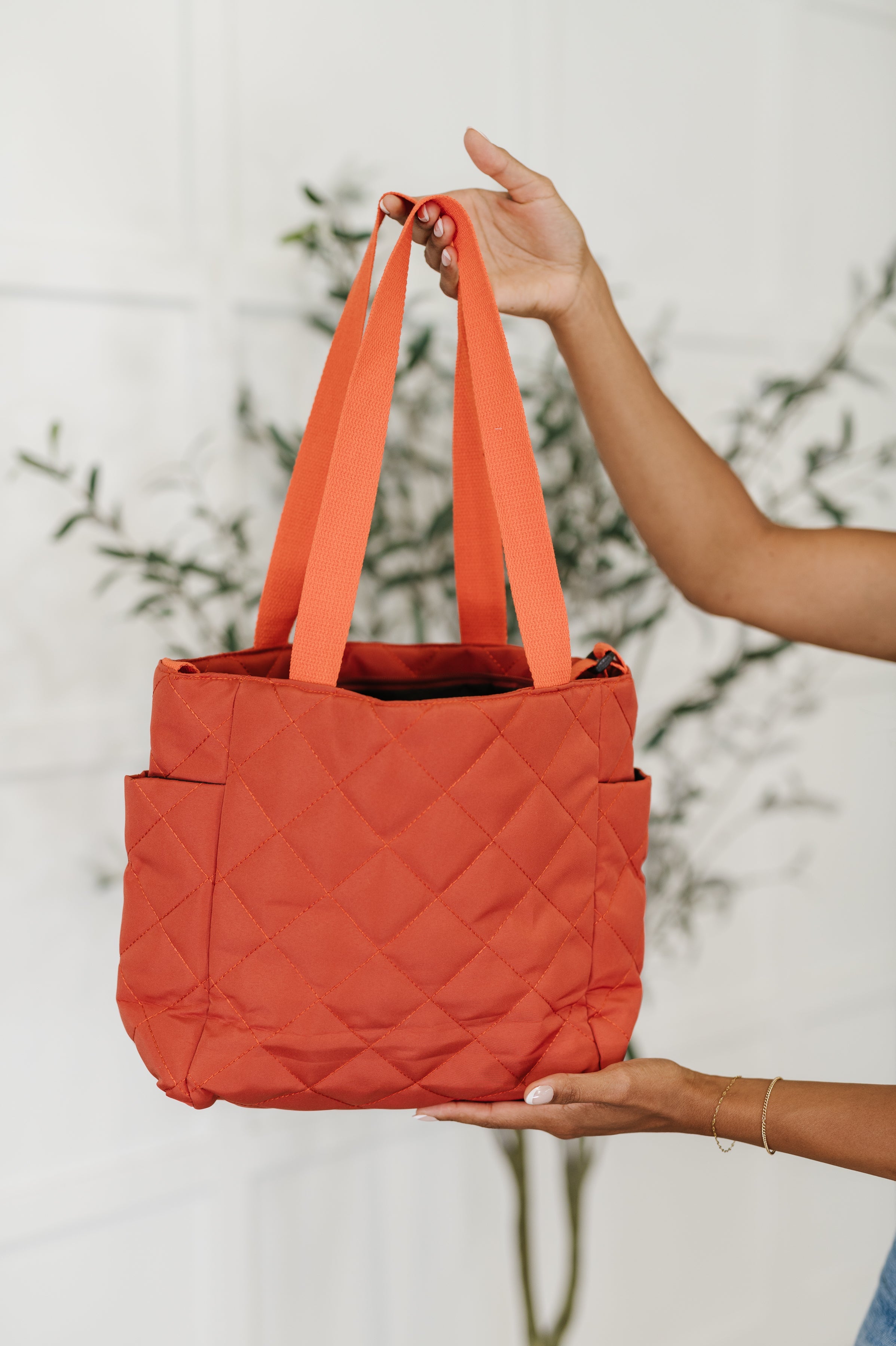Person holding an orange quilted tote bag against a blurred natural background