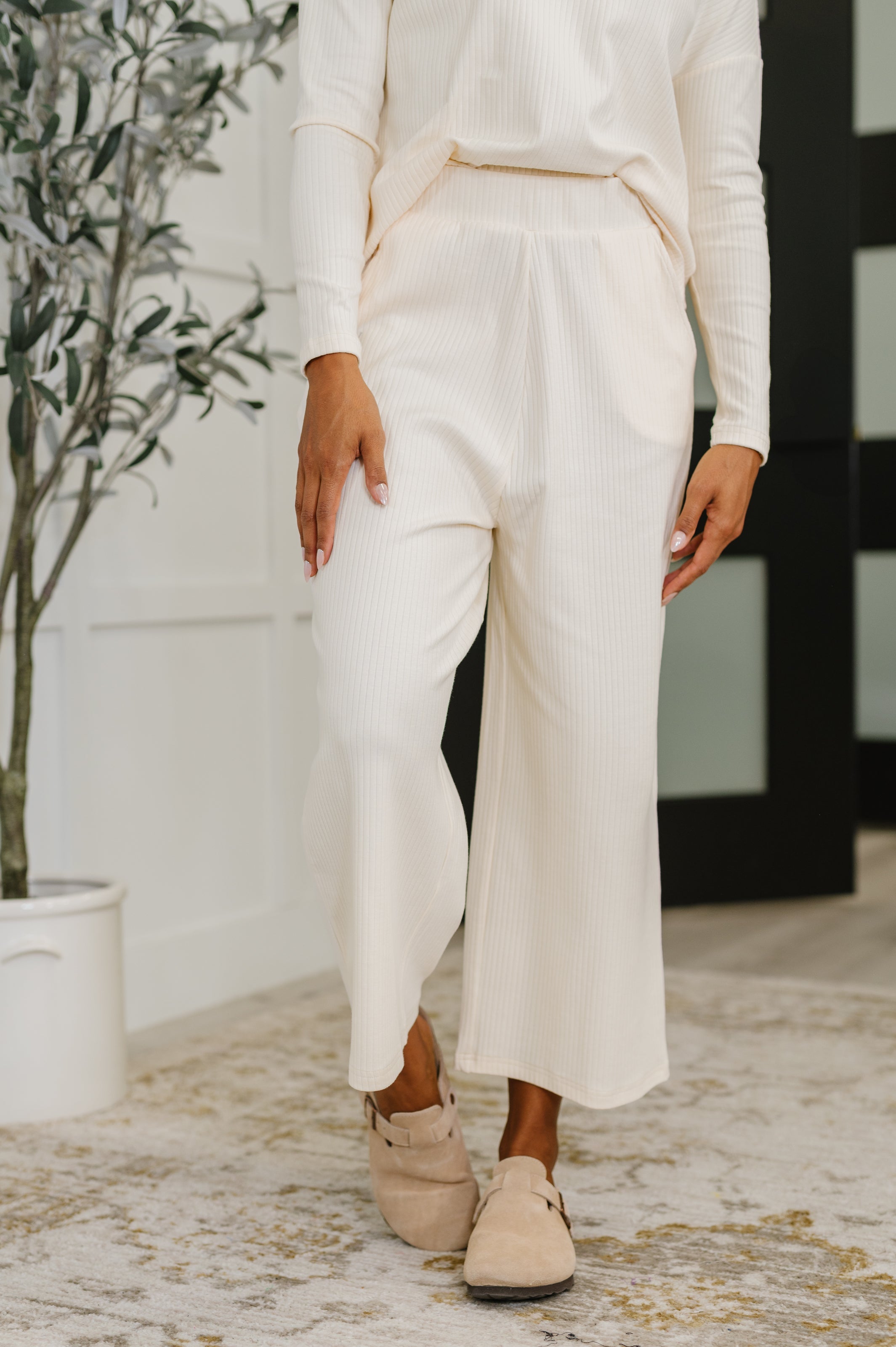 Woman wearing a white outfit with wide-leg pants in an indoor setting.