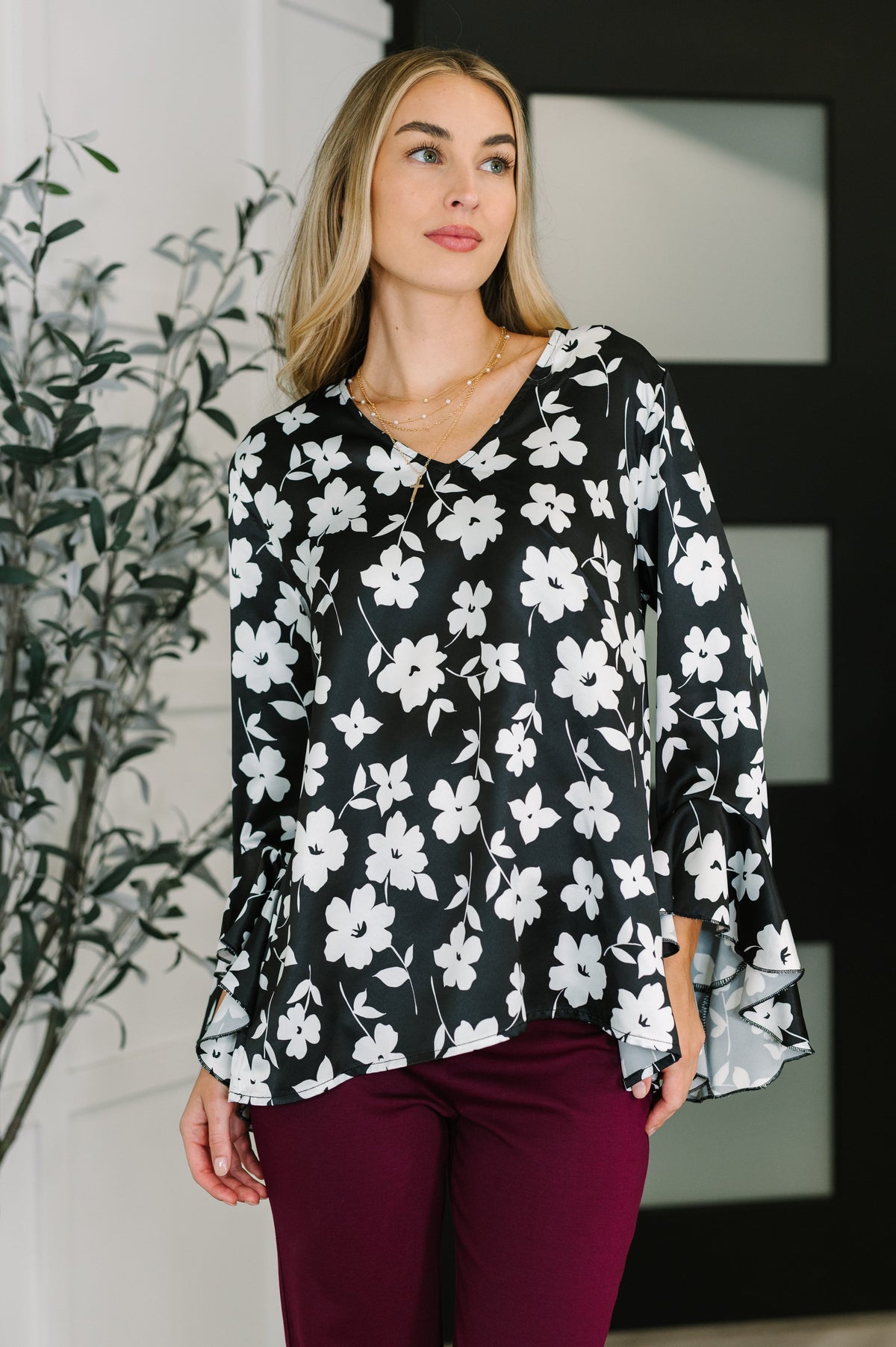 Woman wearing a black and white floral blouse with V-neckline and ruffled sleeves.