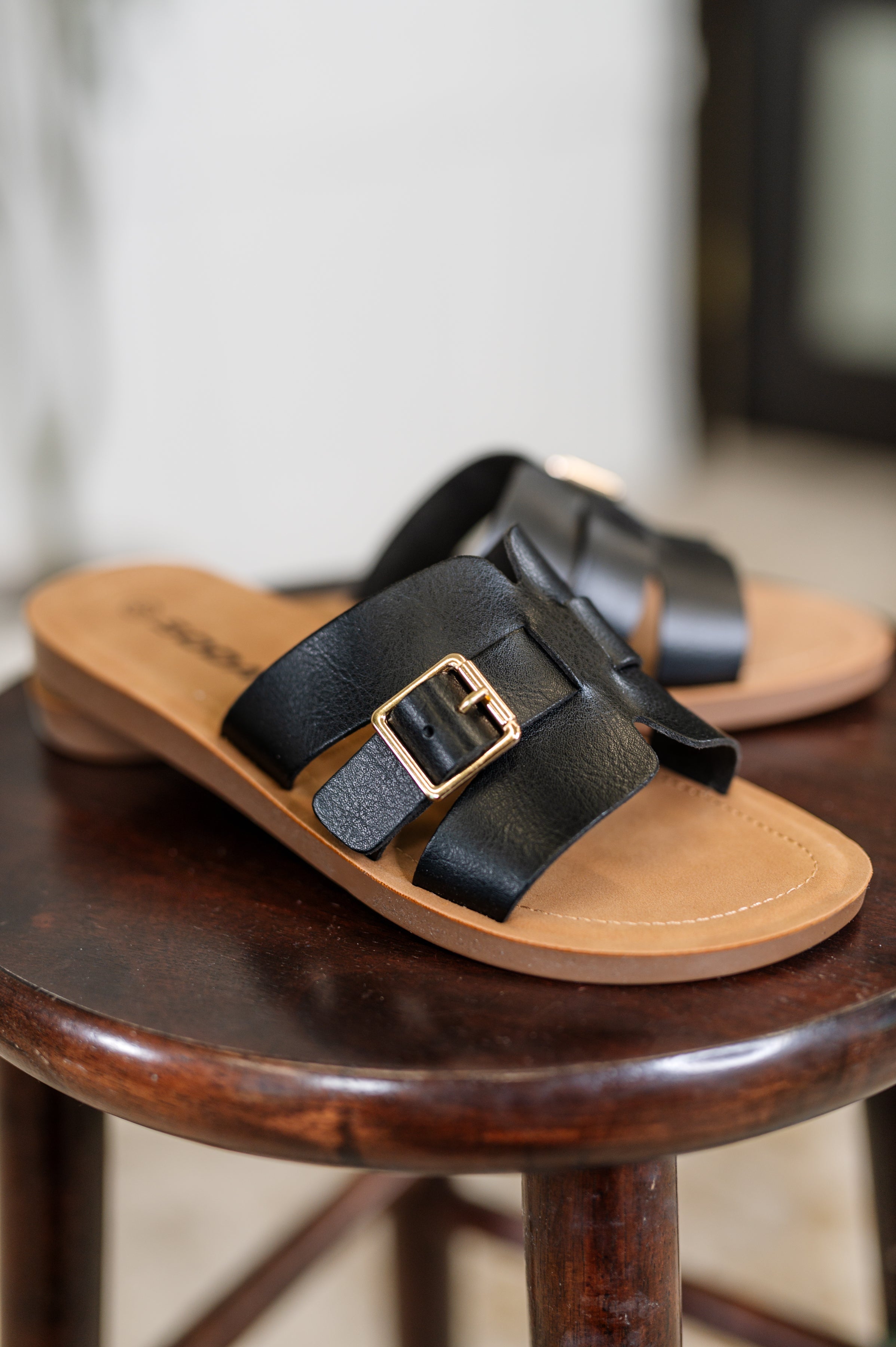 Women's black sandals with a gold buckle on a wooden stool