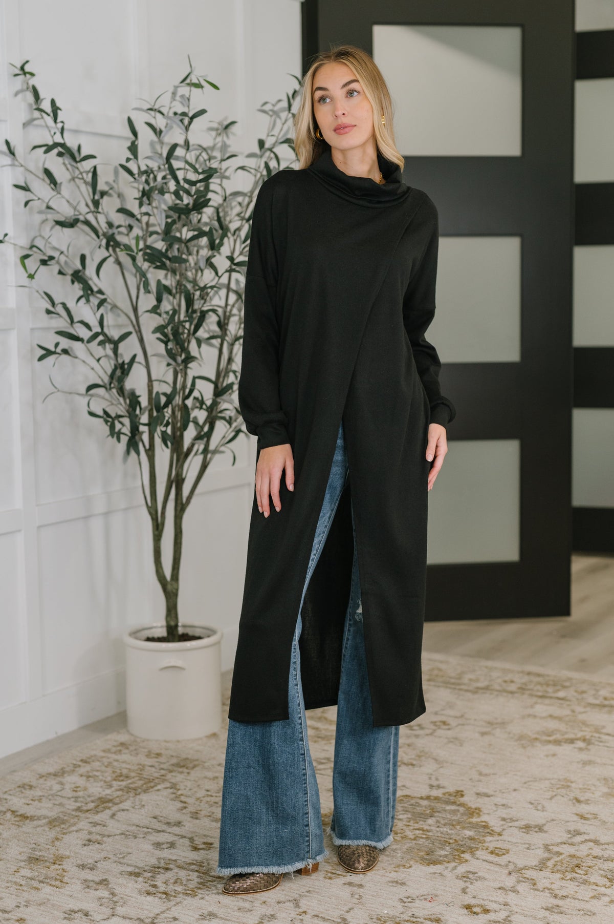 Black turtleneck tunic with drop shoulders and banded cuffs, worn by a model paired with jeans.