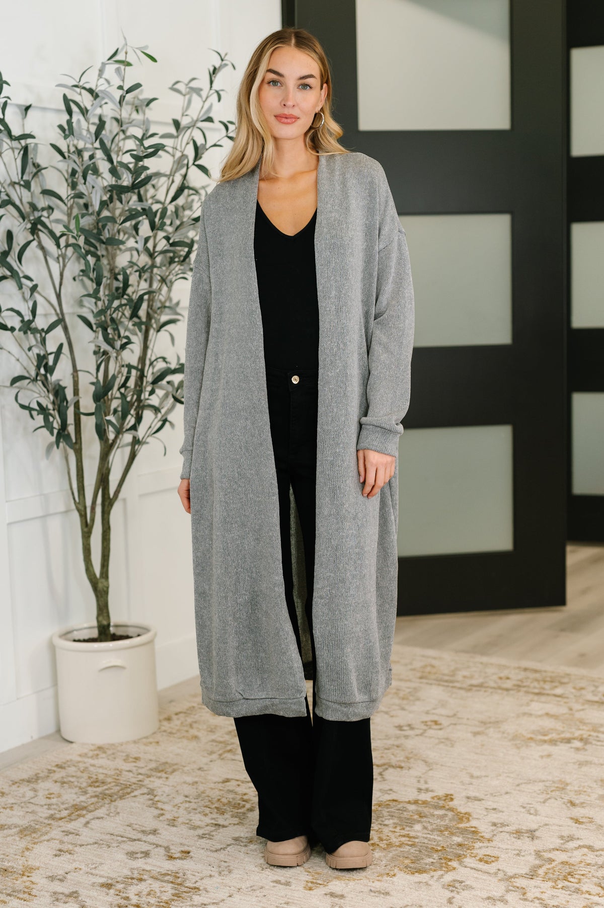 Woman wearing a soft grey open front cardigan with drop shoulder design and banded cuffs.