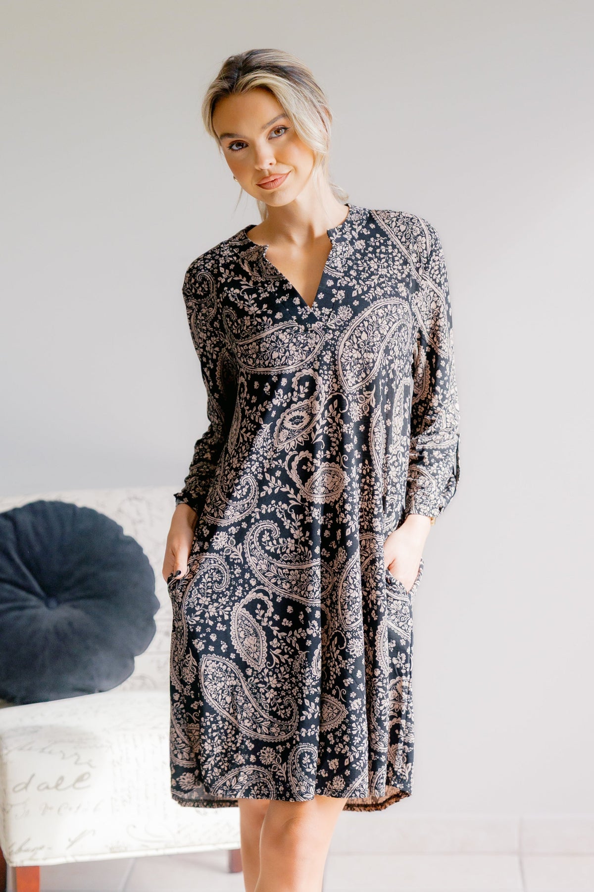 A woman wearing a black dress with a beige paisley pattern, featuring a Lizzy neck and A-line silhouette.
