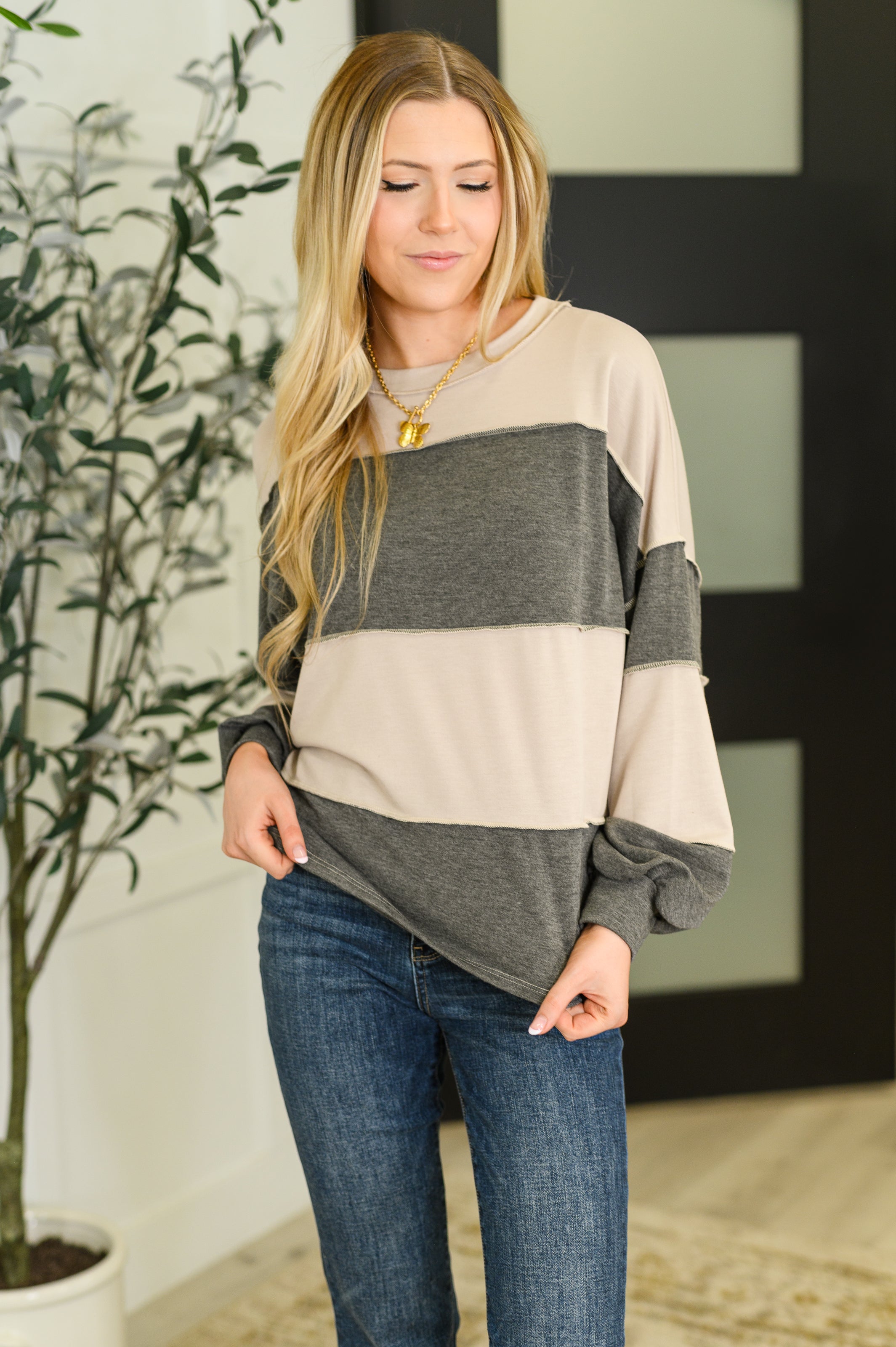 Woman wearing a beige and gray color-blocked shirt with blue jeans indoors.
