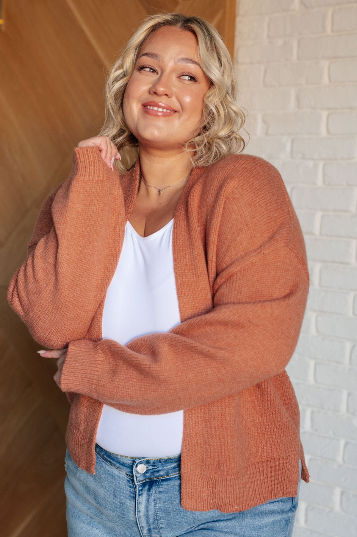 Woman wearing a rust-colored open front cardigan with drop shoulders and ribbed hemline.