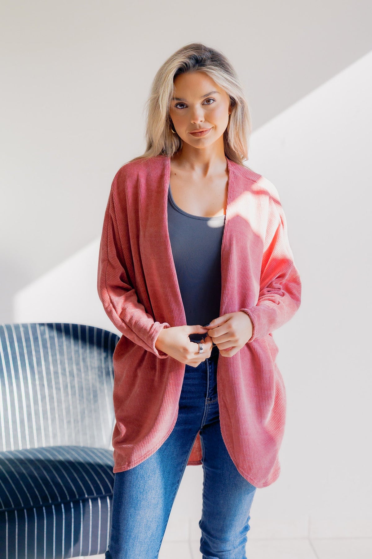 A woman wearing a pink cardigan over a gray top with blue jeans.
