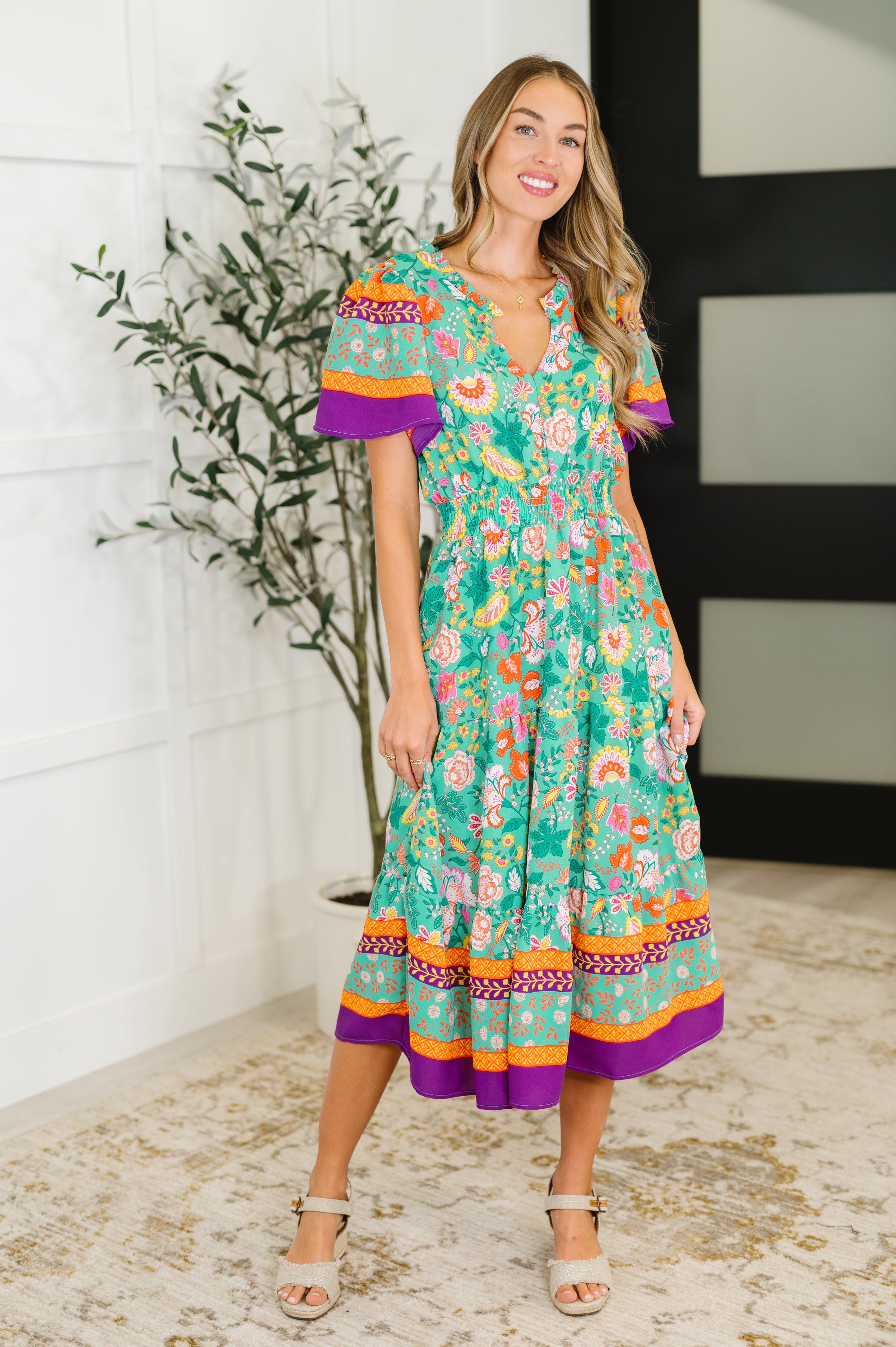 Woman wearing a colorful floral dress with bell sleeves in an indoor setting.
