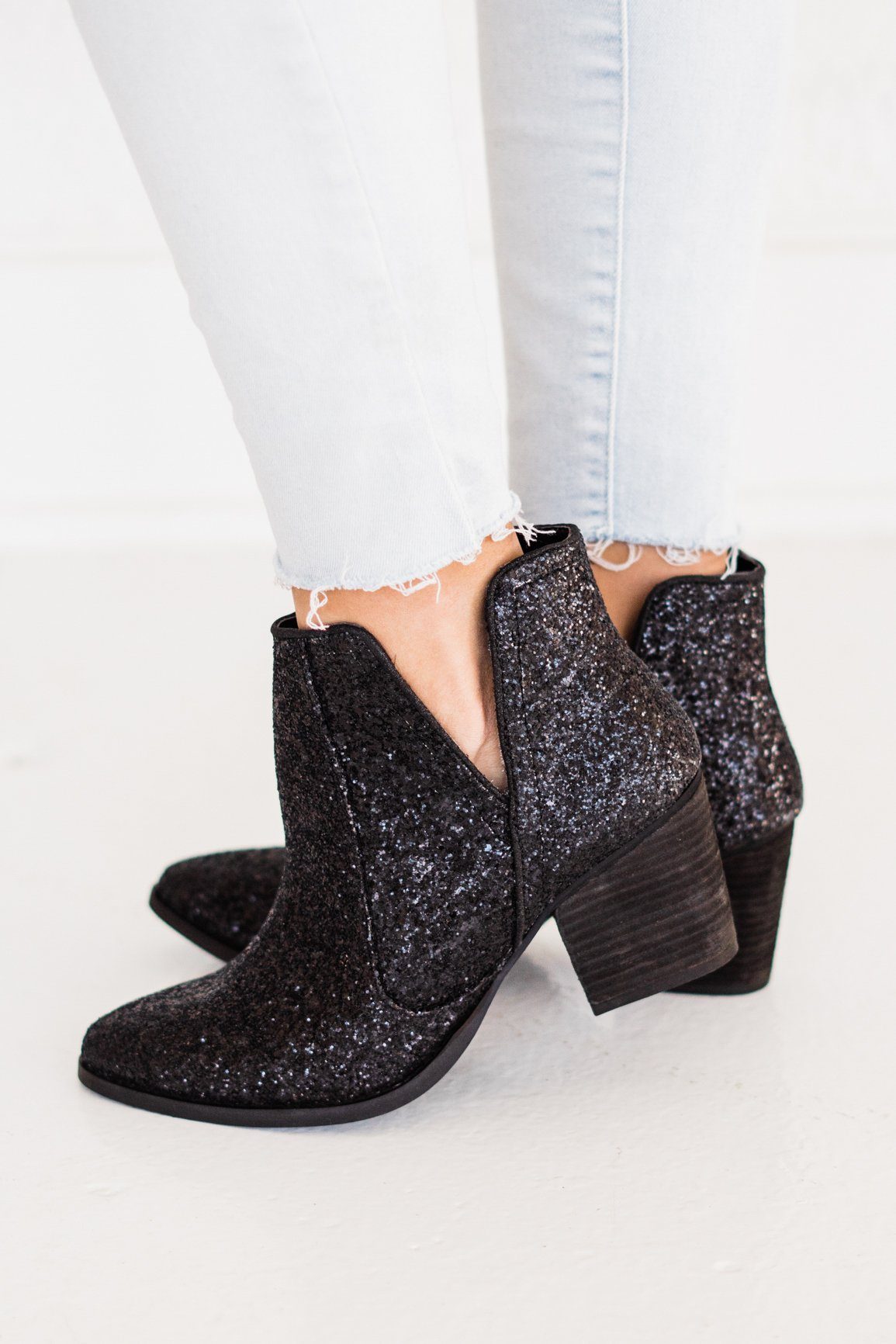 A woman wearing black glitter booties with a rubber heel and sole against a white background.