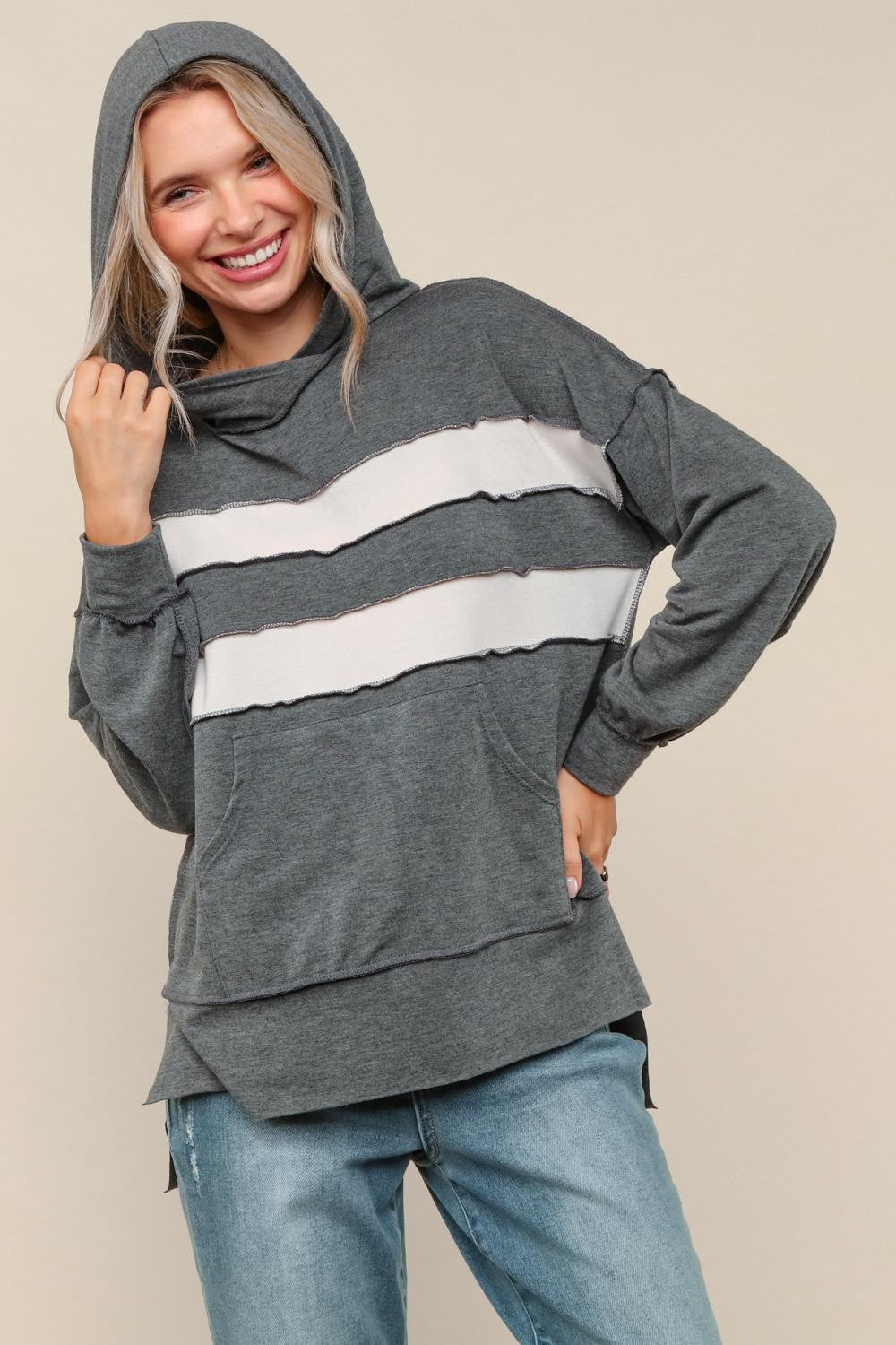Woman wearing a gray hoodie with white stripes and blue jeans on a beige background