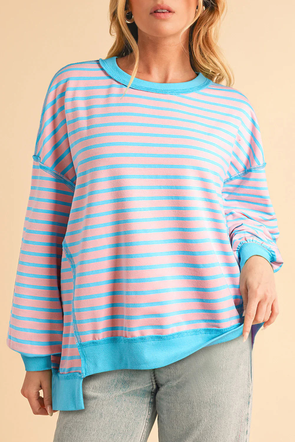 Woman wearing a pink and blue striped sweatshirt against a beige background
