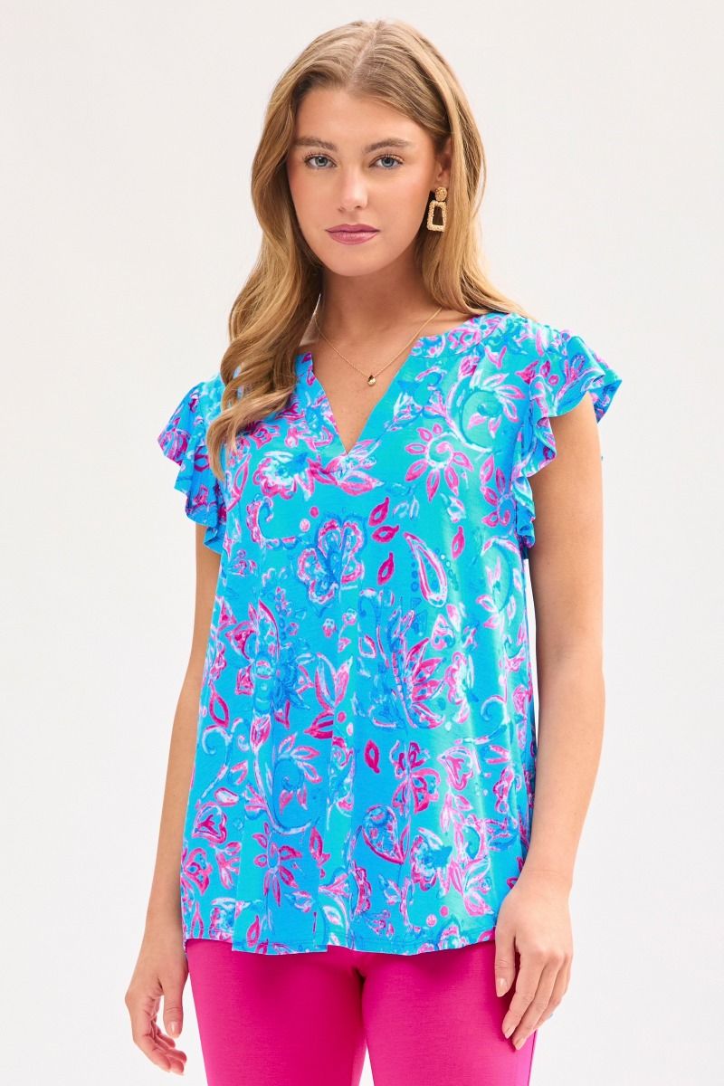 A woman wearing a royal blue top with a floral pattern, featuring a mandarin collar and flutter sleeves.